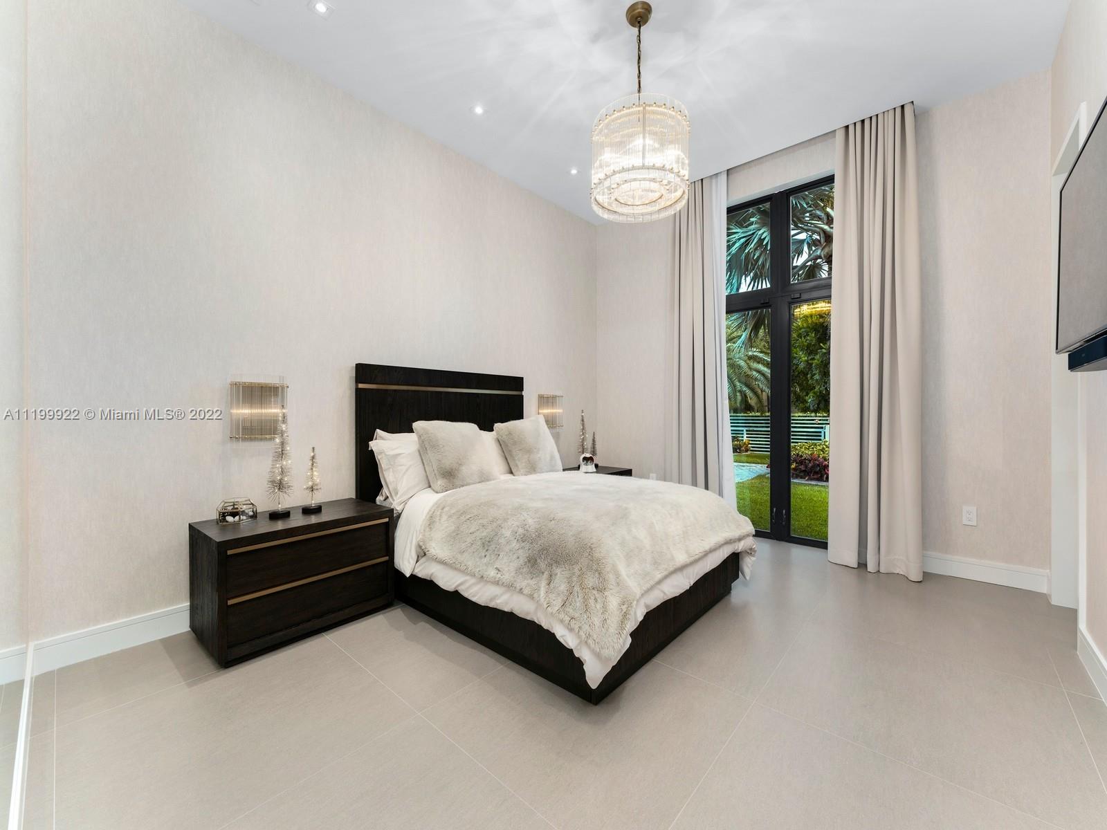 Modern bedroom with a dark wood bed, crystal chandelier, and tall garden-facing windows.