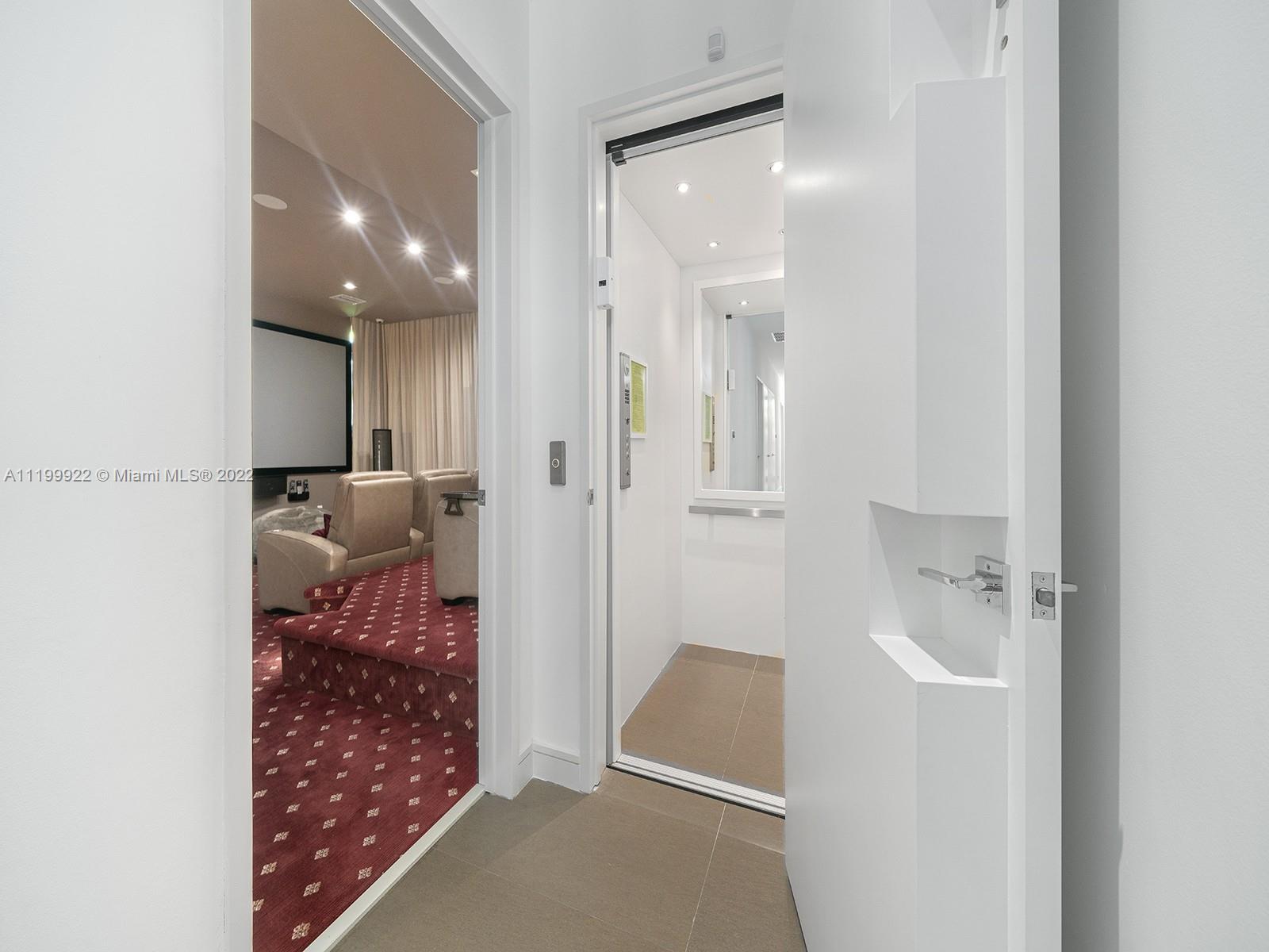 Condo entry with elevator beside a media room with a large screen and patterned red carpet.