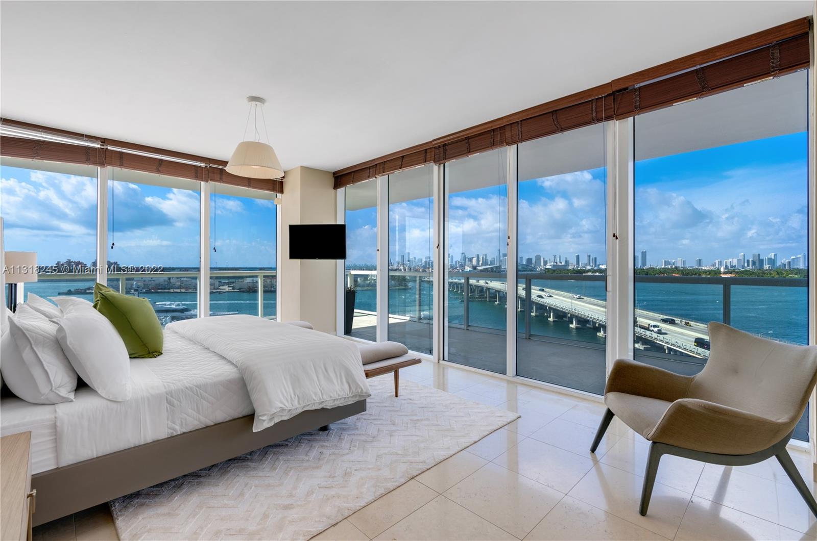 Bedroom with floor-to-ceiling windows overlooking Biscayne Bay, a bridge, and the downtown skyline.