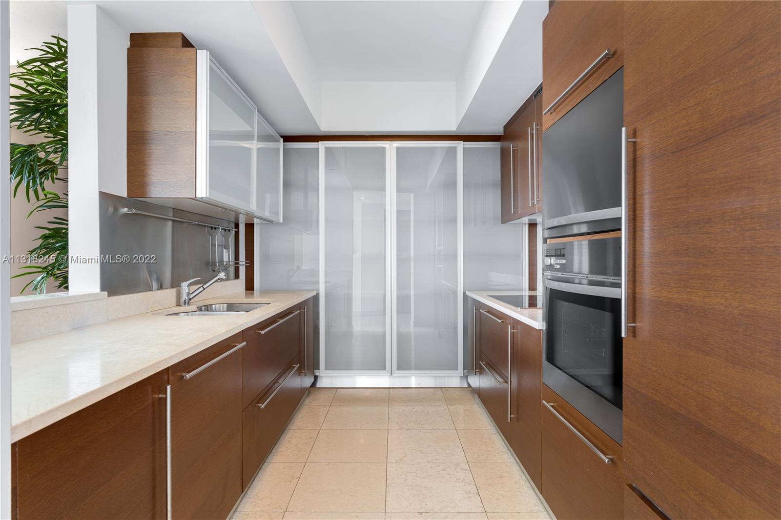 Modern kitchen with warm wood cabinetry, pale stone counters, and frosted glass pantry doors.