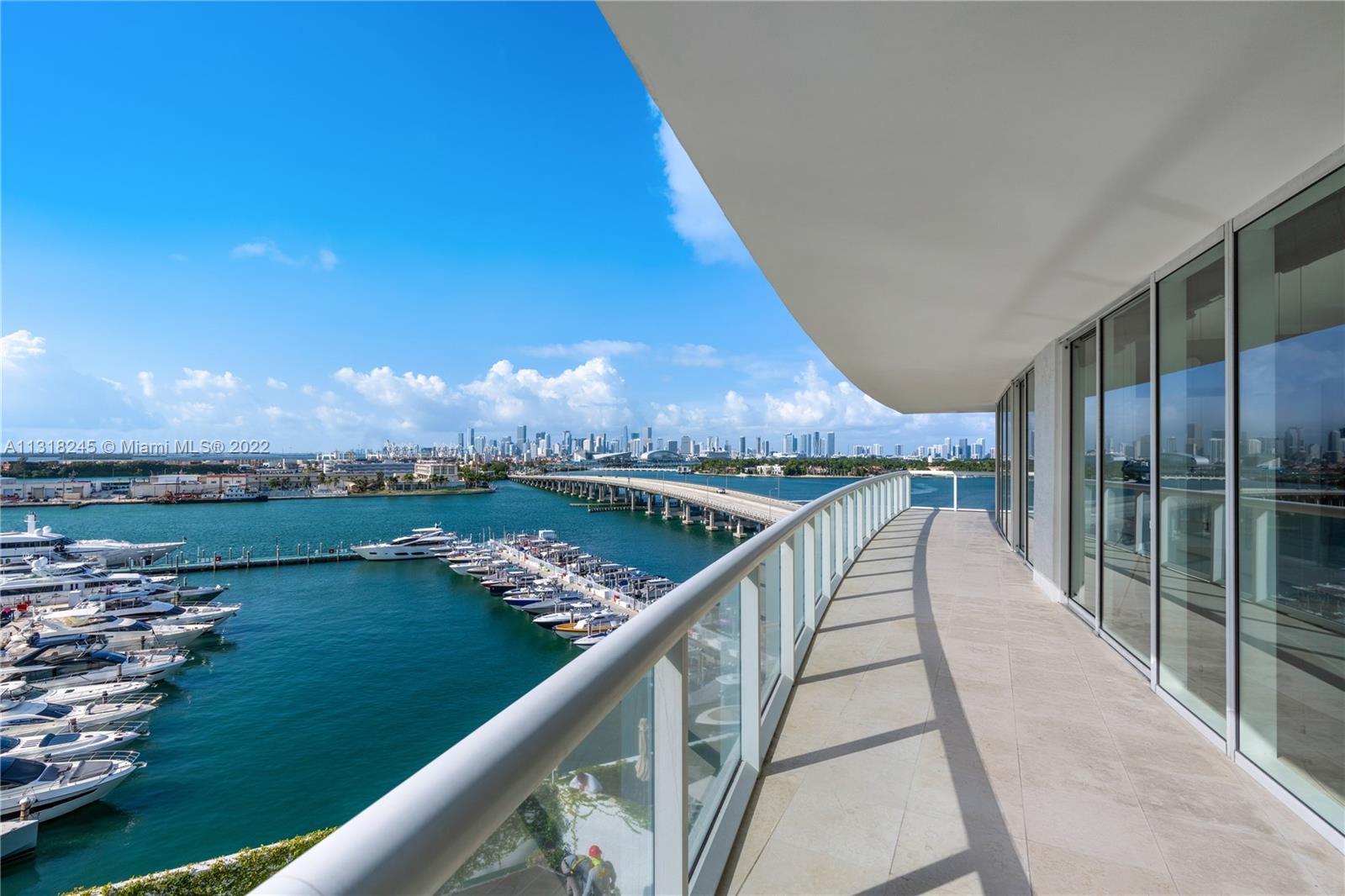 Curved glass-railed balcony overlooking a marina, bridge, and Miami skyline.