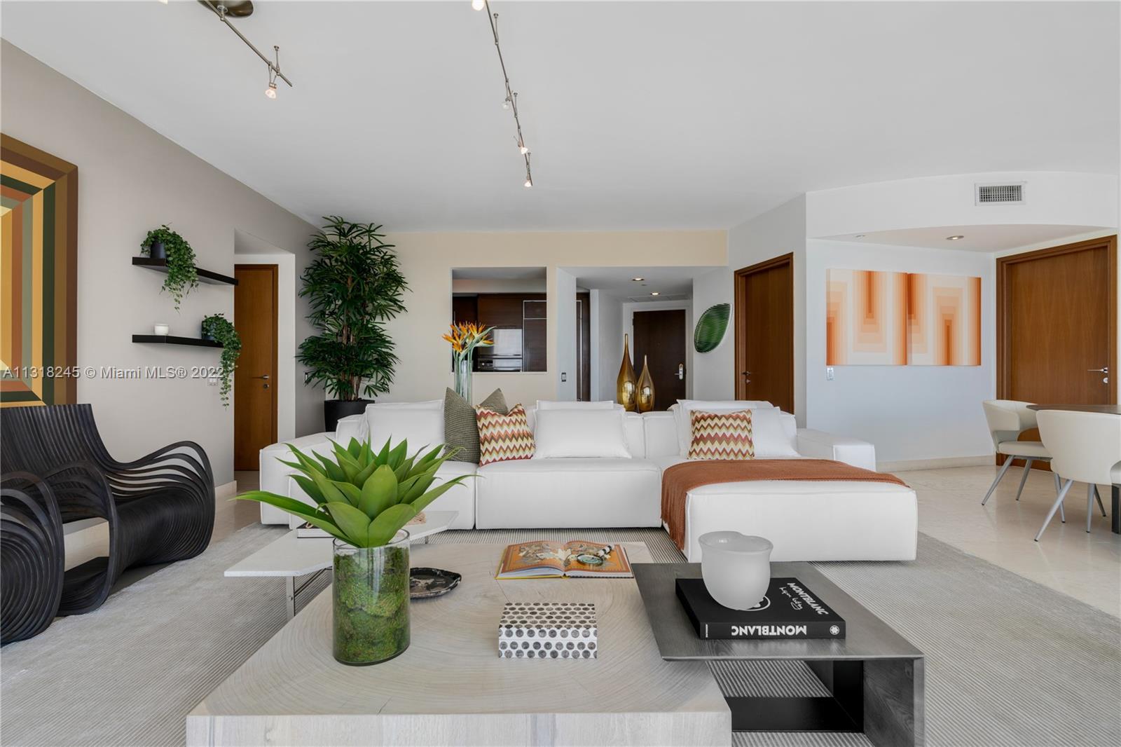 Furnished condo living room with a white sectional, black sculptural chairs, and contemporary artwork.