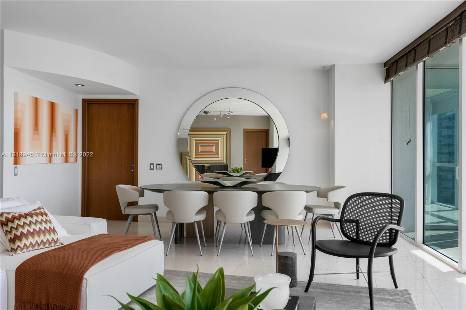 Condo living and dining area with a white sofa, oval table, and sliding glass doors to a balcony.