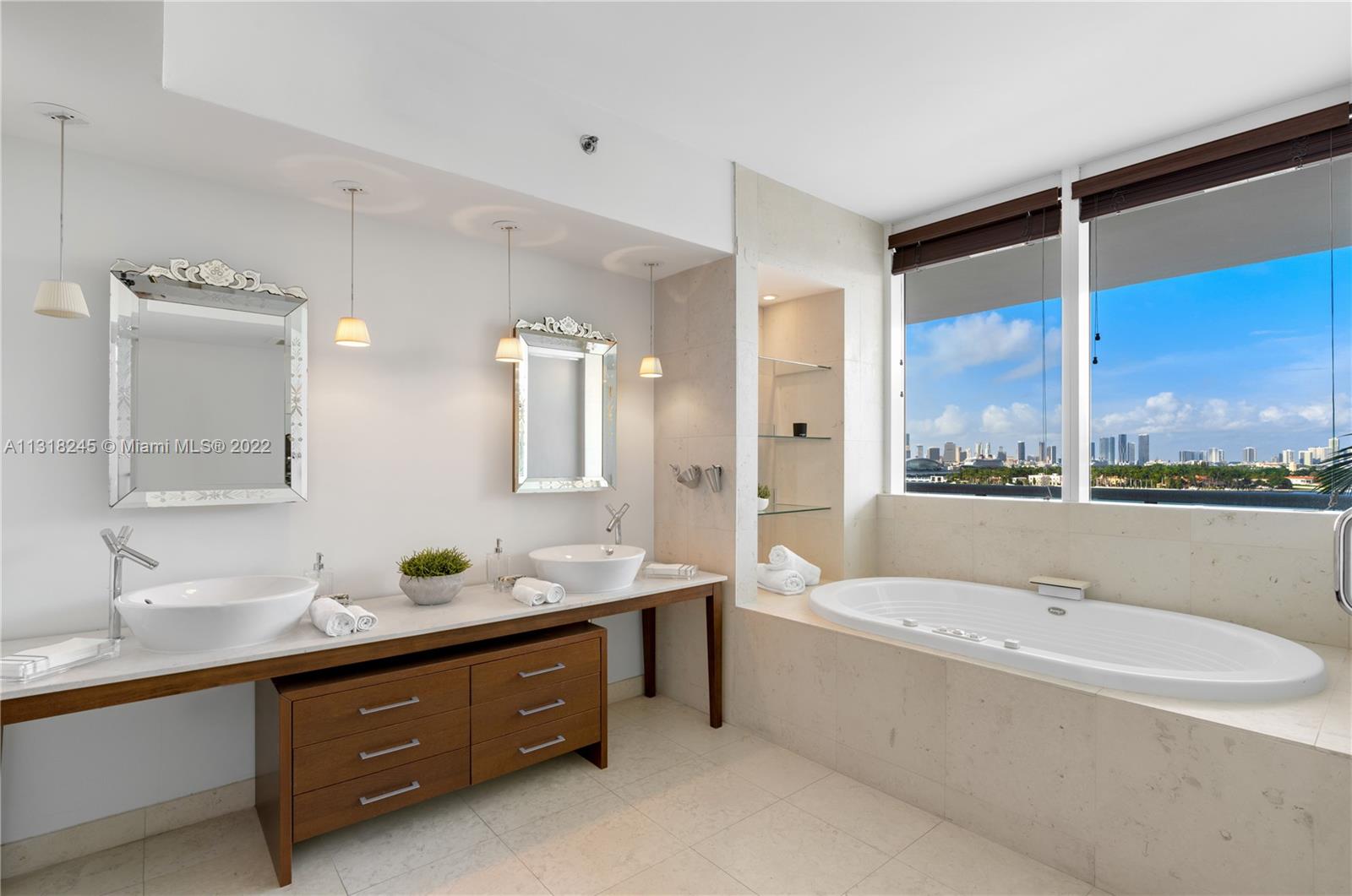 Modern bathroom with a double vanity and soaking tub overlooking the water and Miami skyline.