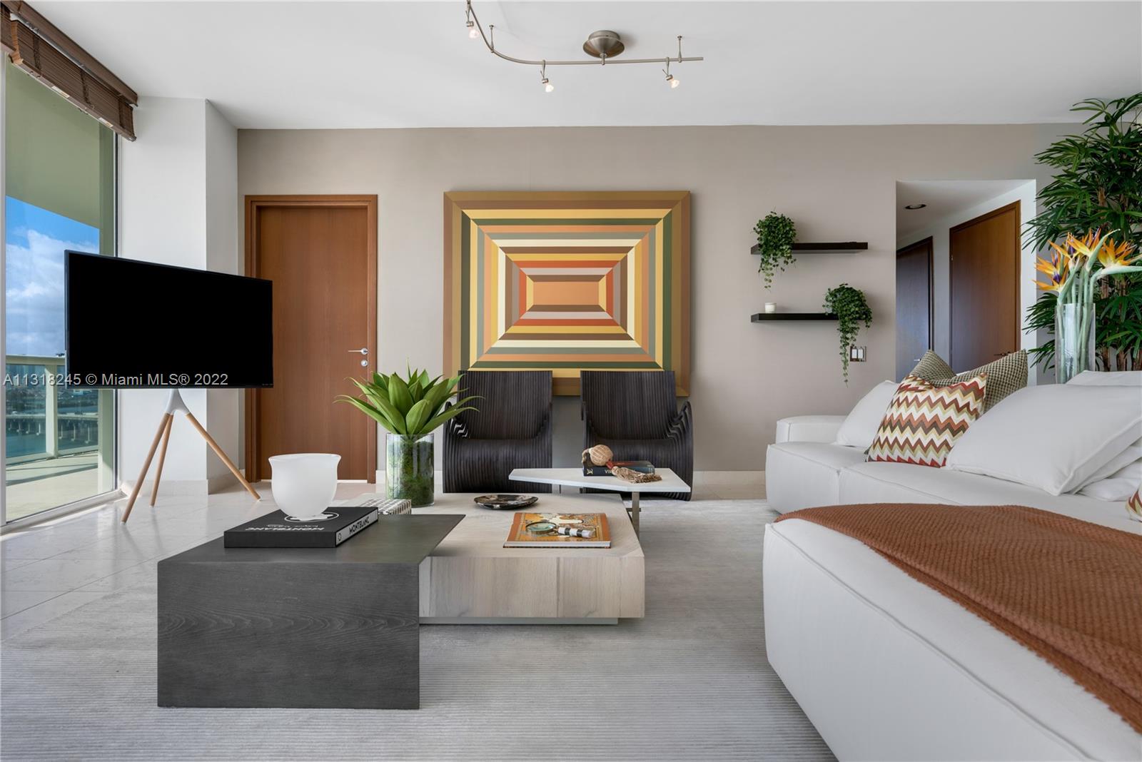 Furnished living room with a white sectional, dark lounge chairs, and colorful geometric wall art.