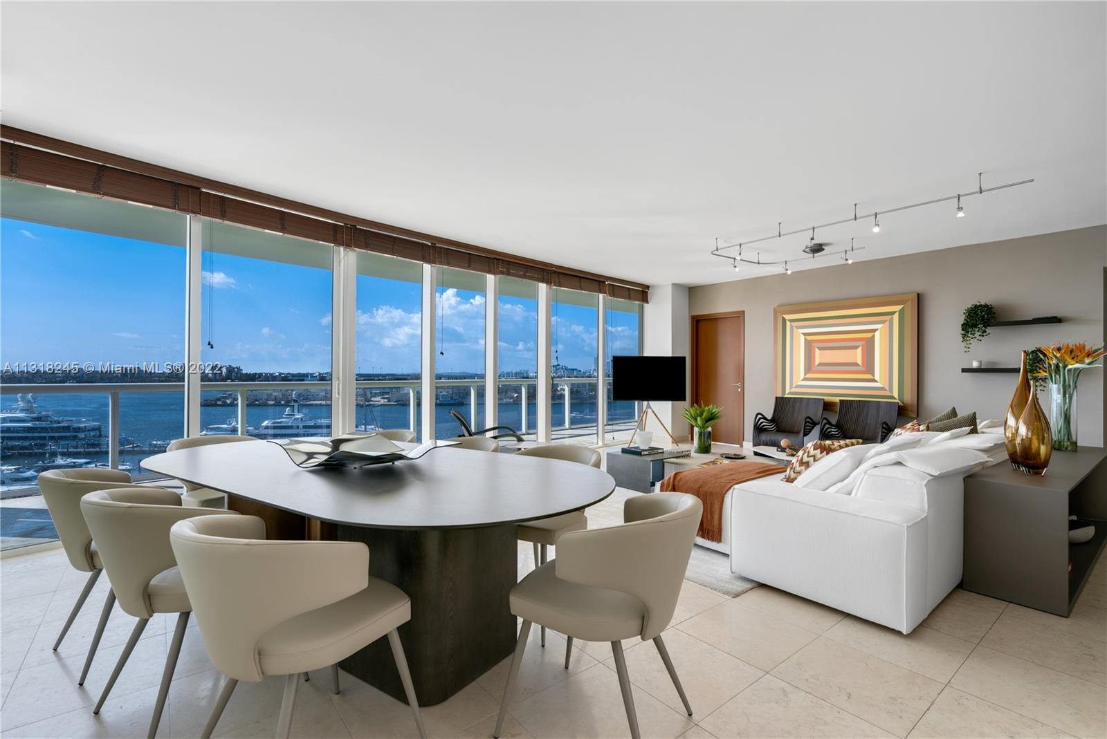 Furnished living and dining area with floor-to-ceiling windows overlooking a marina and blue water.