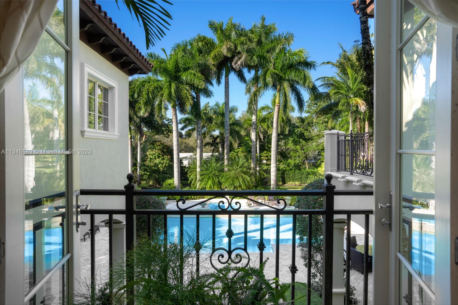 Balcony view over a swimming pool and tropical landscaping framed by open doors.