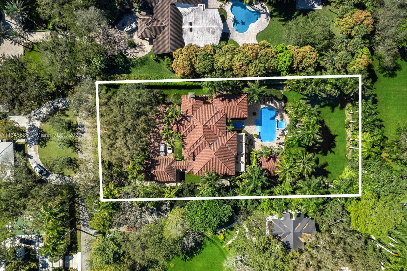 Aerial view of a red-tile-roofed home and swimming pool within a lush, outlined lot.