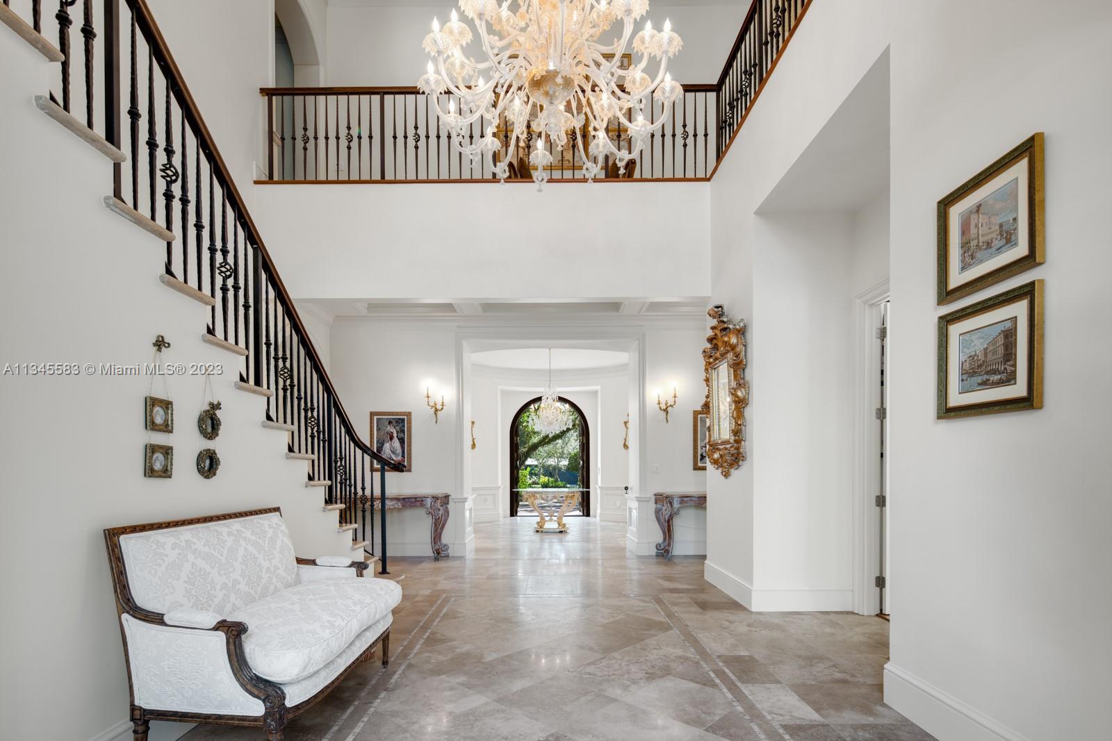 Two-story foyer with a sweeping staircase, chandelier, marble floor, and arched glass front door.
