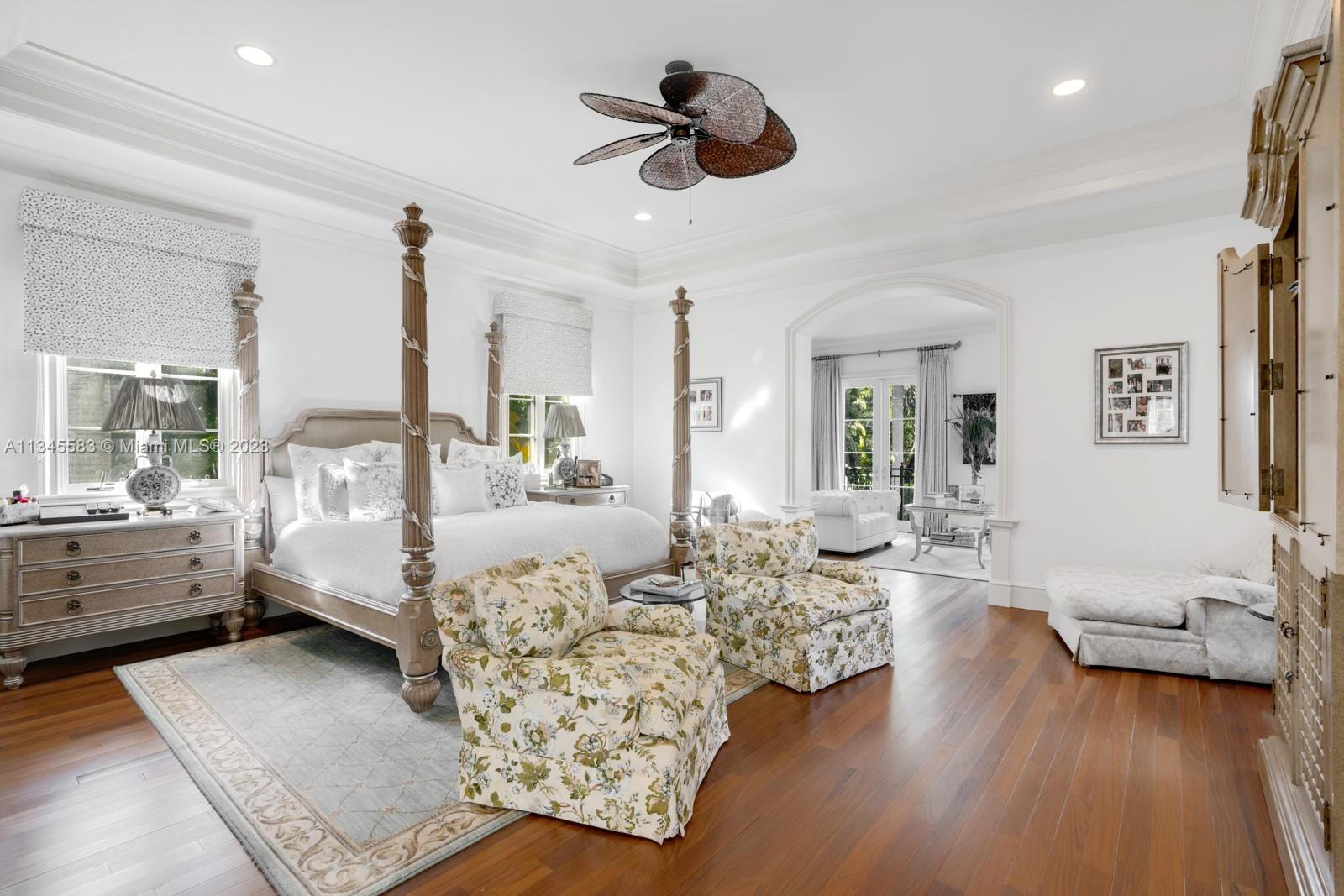 Bedroom with a carved four-poster bed, floral armchairs, and an adjoining sitting area.