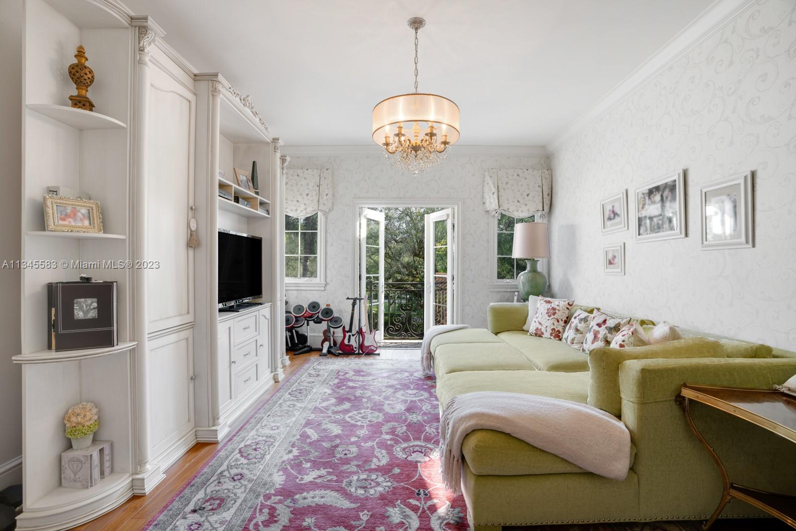 Living room with a pale green sectional, built-in shelving, patterned rug, and open doors to a balcony.