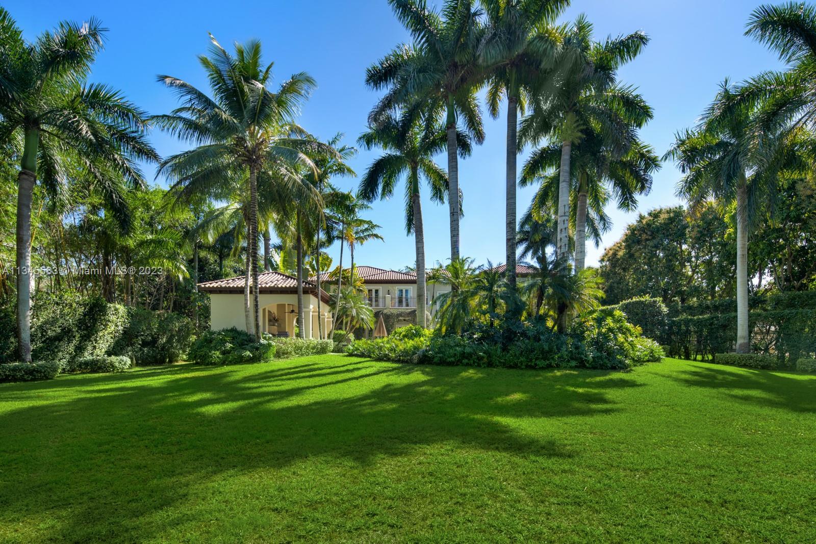Two-story home with a tile roof behind a broad lawn and tall palms.