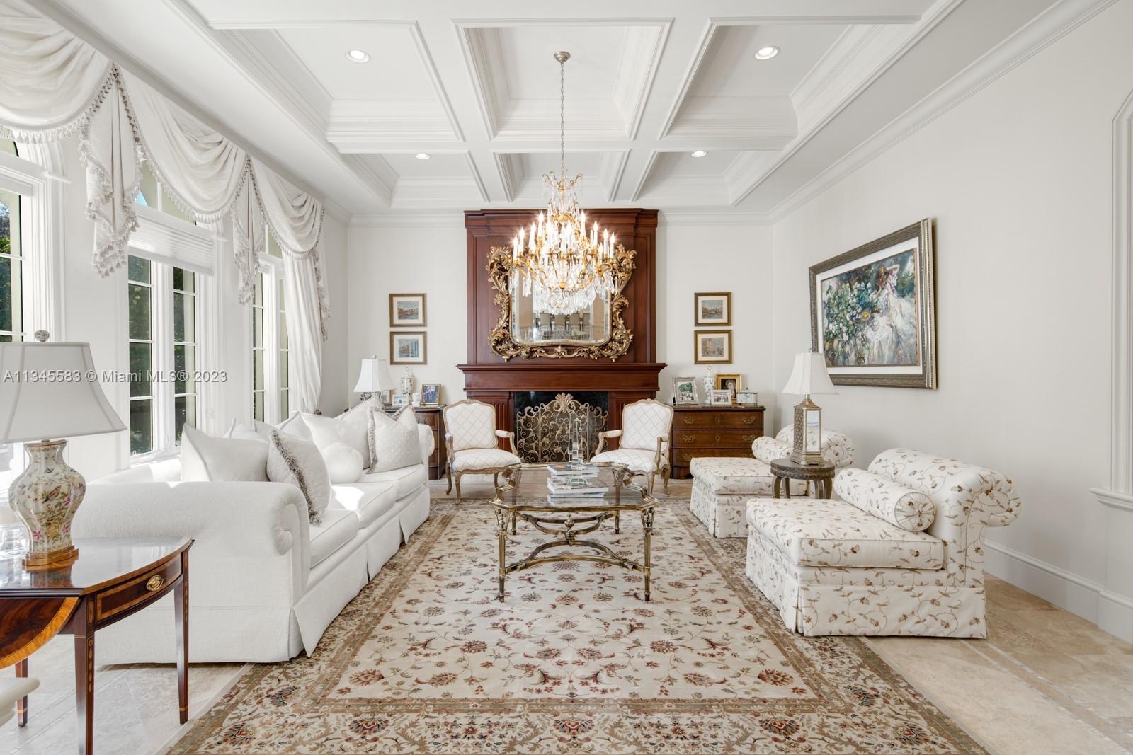 Formal living room with an ornate fireplace, crystal chandelier, and coffered ceiling.
