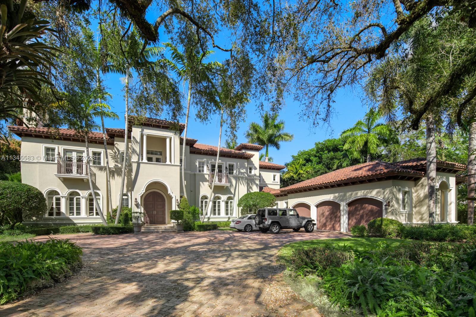 Two-story Mediterranean-style home with an arched entrance, tile-roofed garage, and cars on a brick driveway.