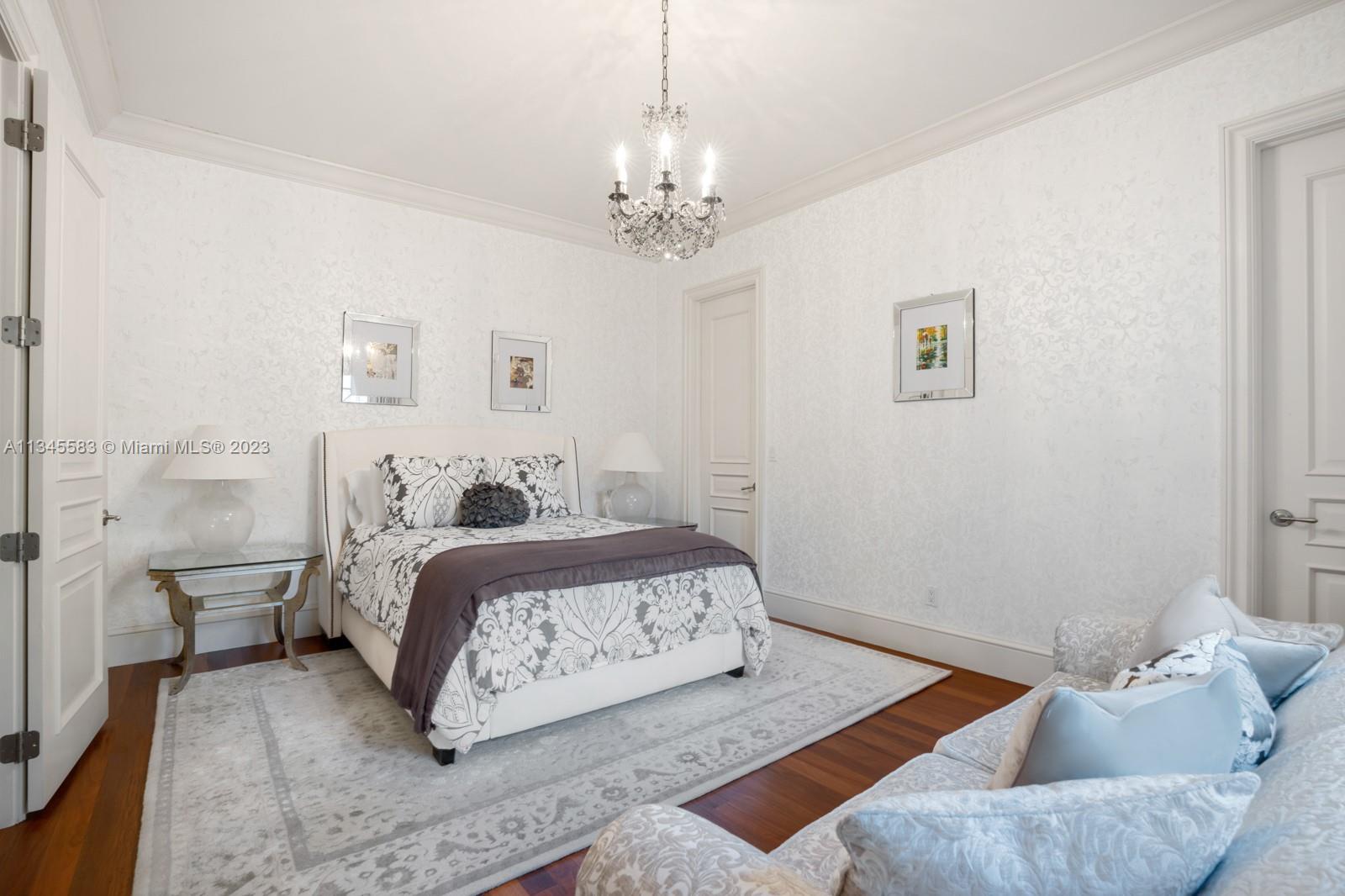 Bedroom with a floral-patterned bed, crystal chandelier, patterned wallpaper, and hardwood floor.