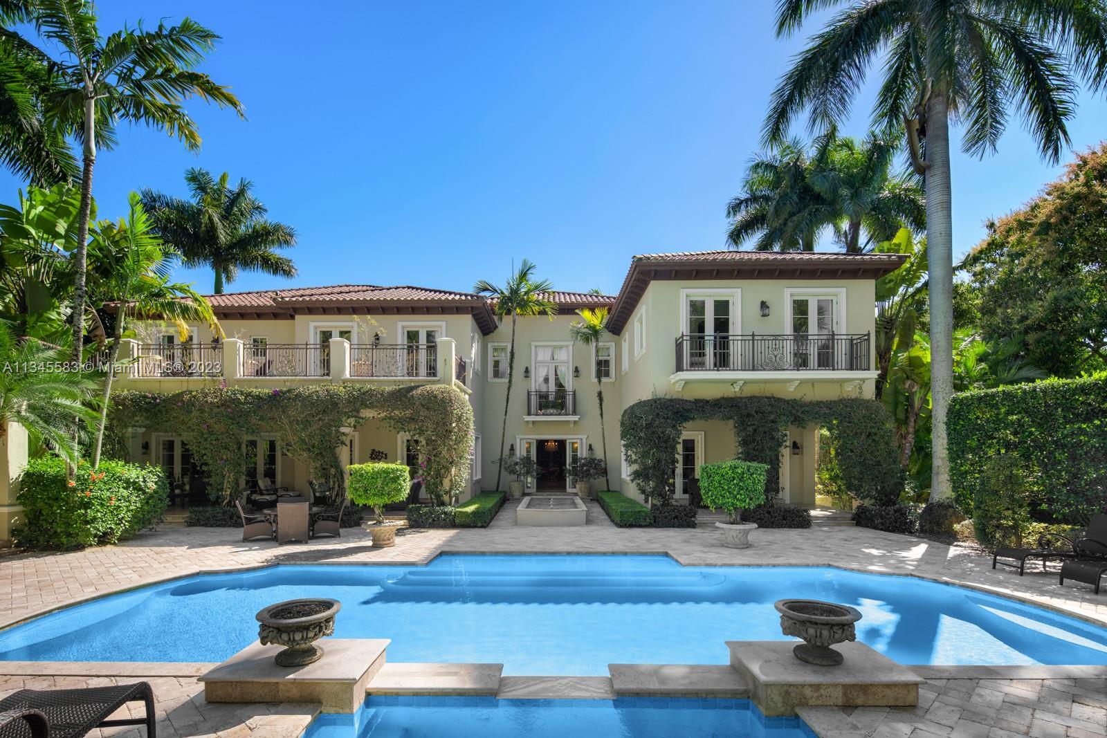 Two-story cream home with a red tile roof and palm-lined pool patio.