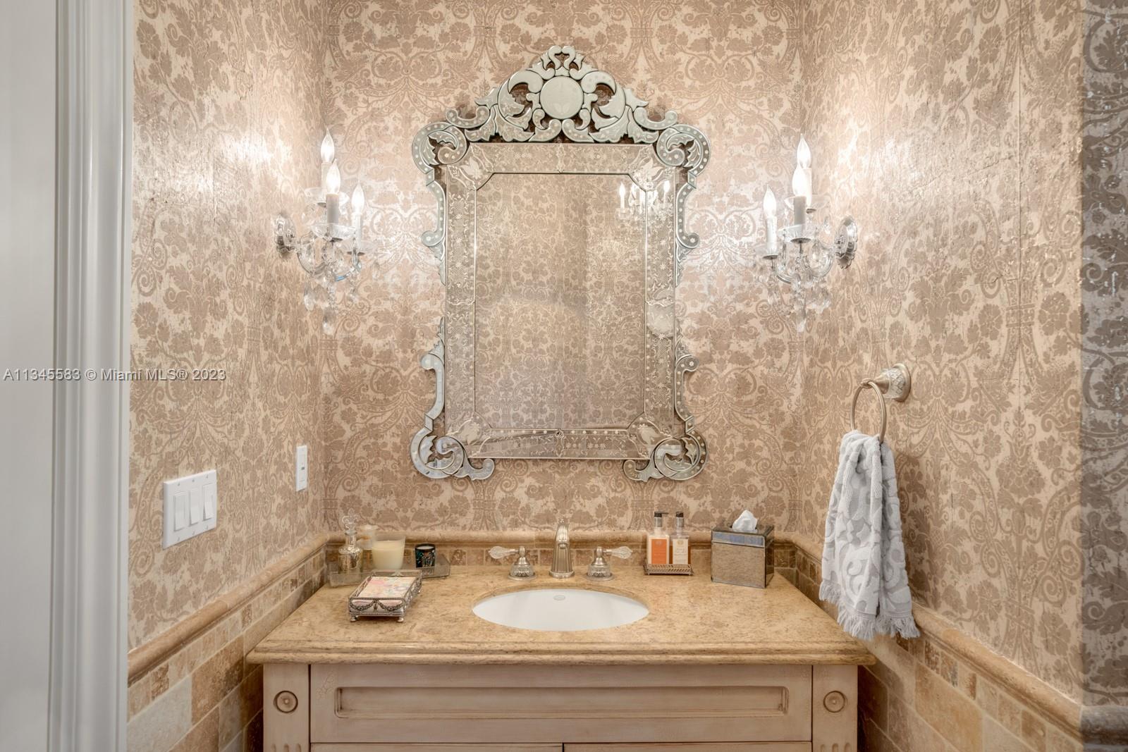 Bathroom vanity with ornate patterned wallpaper, a carved mirror, and crystal sconces.