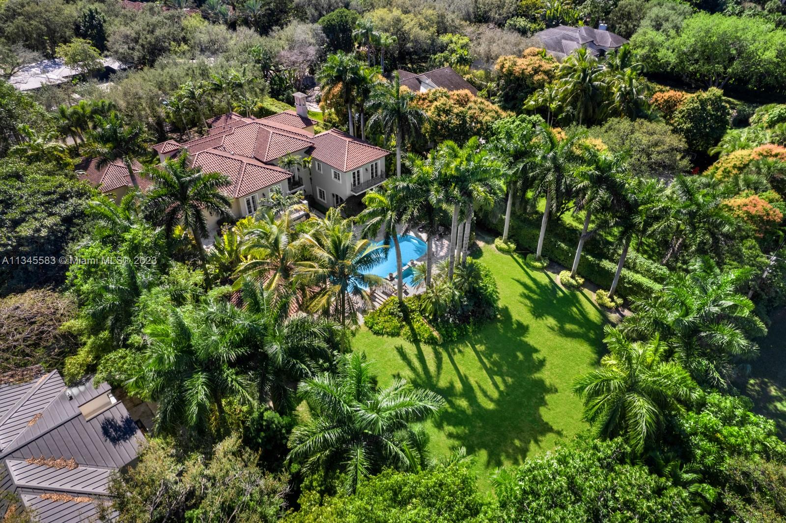 Aerial view of a two-story home with a pool, expansive lawn, and tropical landscaping.