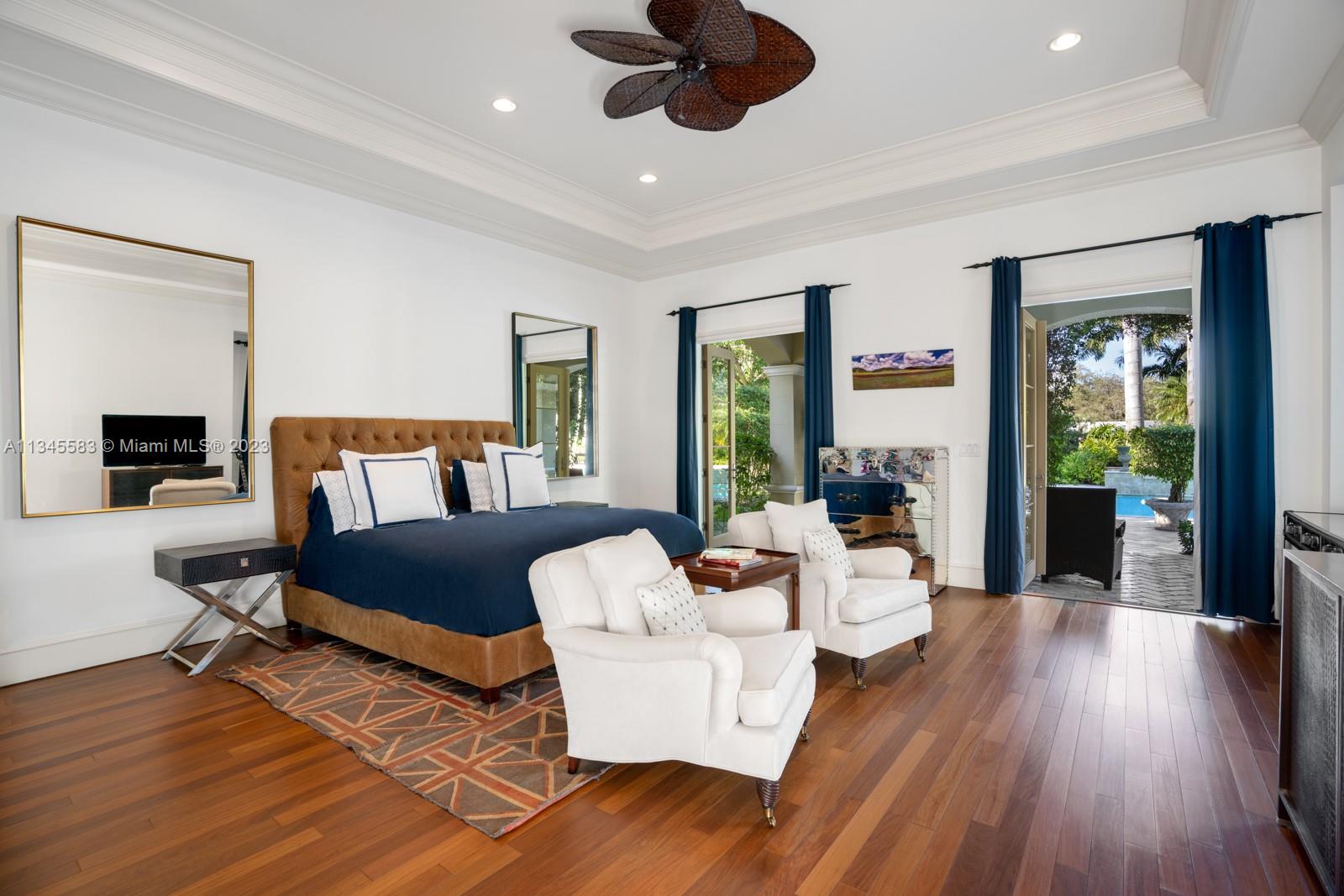 Furnished bedroom with a navy-and-white bed, white armchairs, and open doors to a pool.