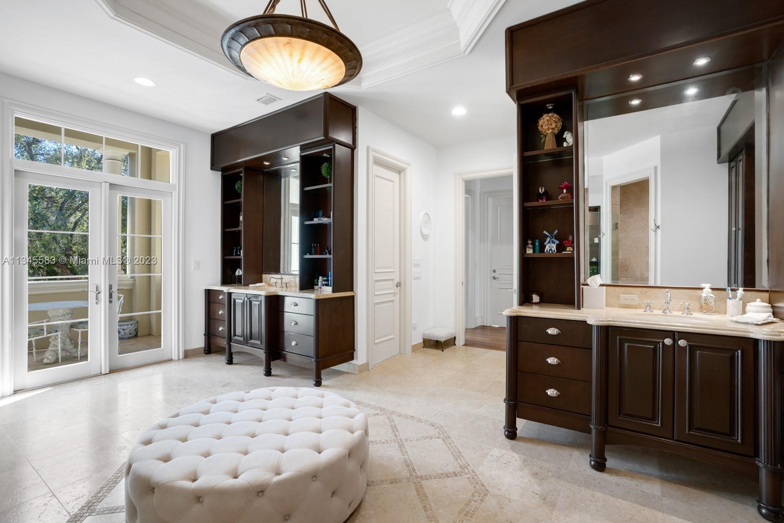 Bathroom with dark wood vanities, pale stone floors, and French doors opening to a balcony.