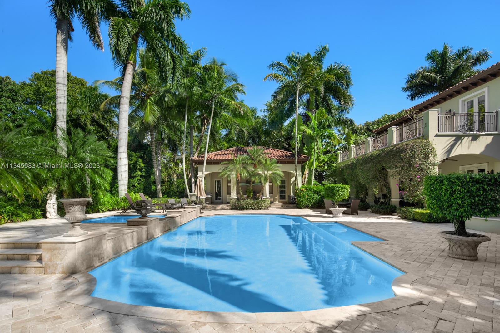 Backyard swimming pool beside a two-story home, surrounded by palm trees and a stone patio.