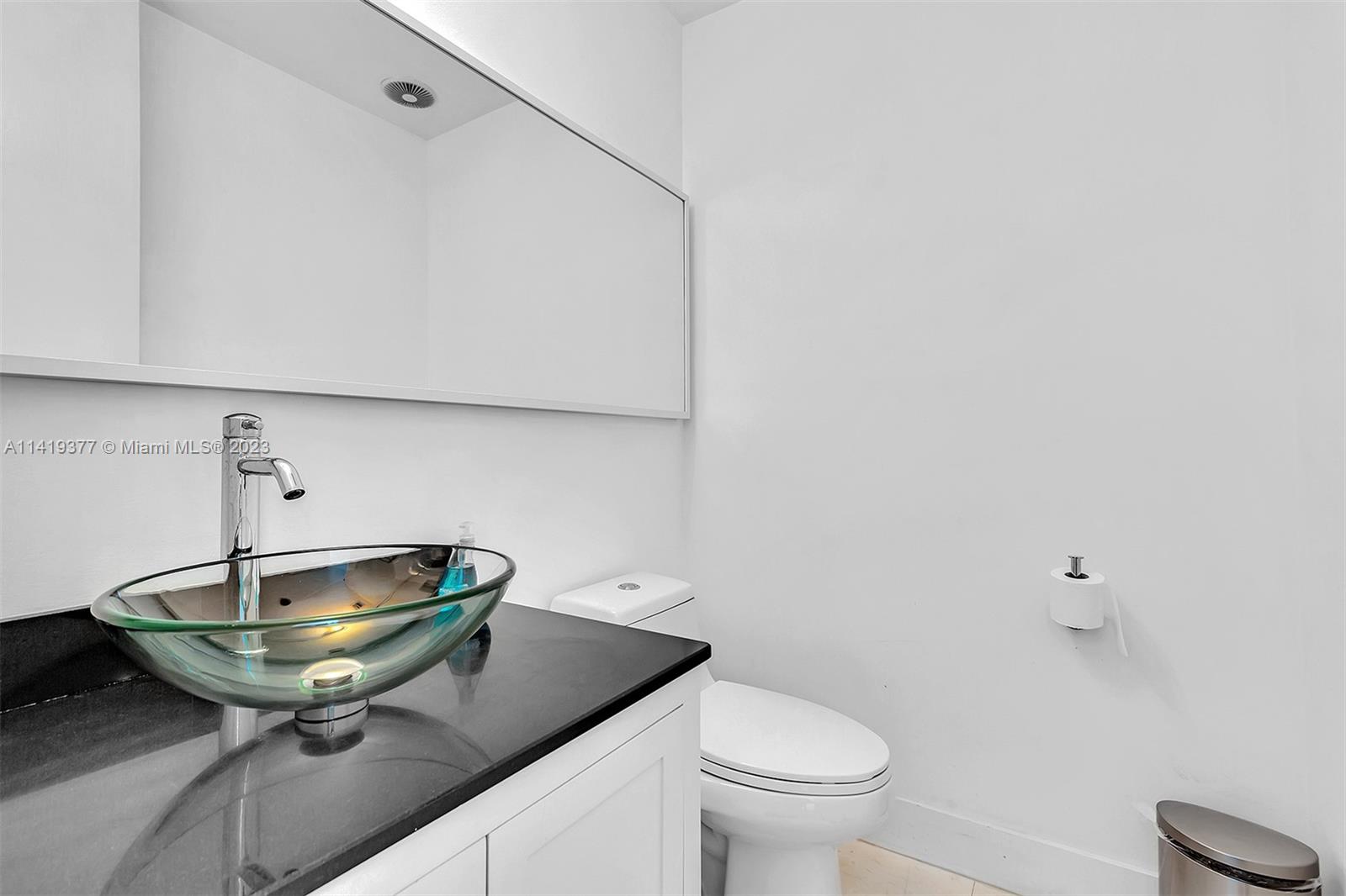 Bathroom with a glass vessel sink, dark countertop, large mirror, and toilet.