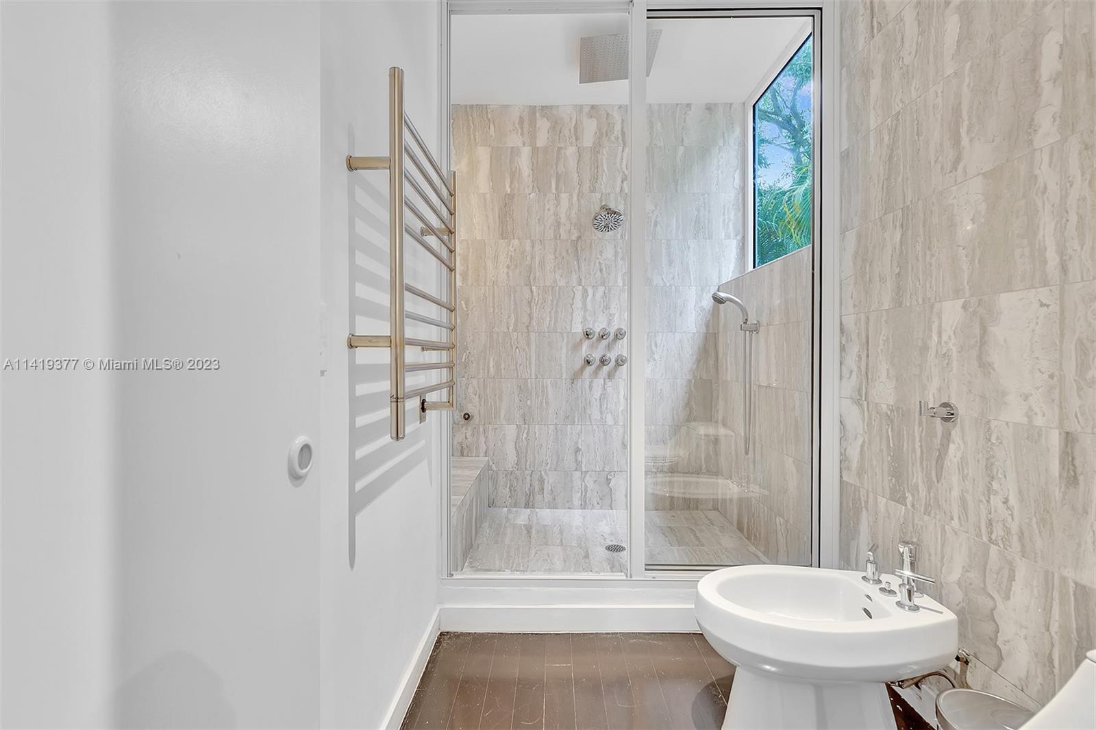 Bathroom with a marble-tiled glass shower, built-in bench, heated towel rack, and pedestal sink.
