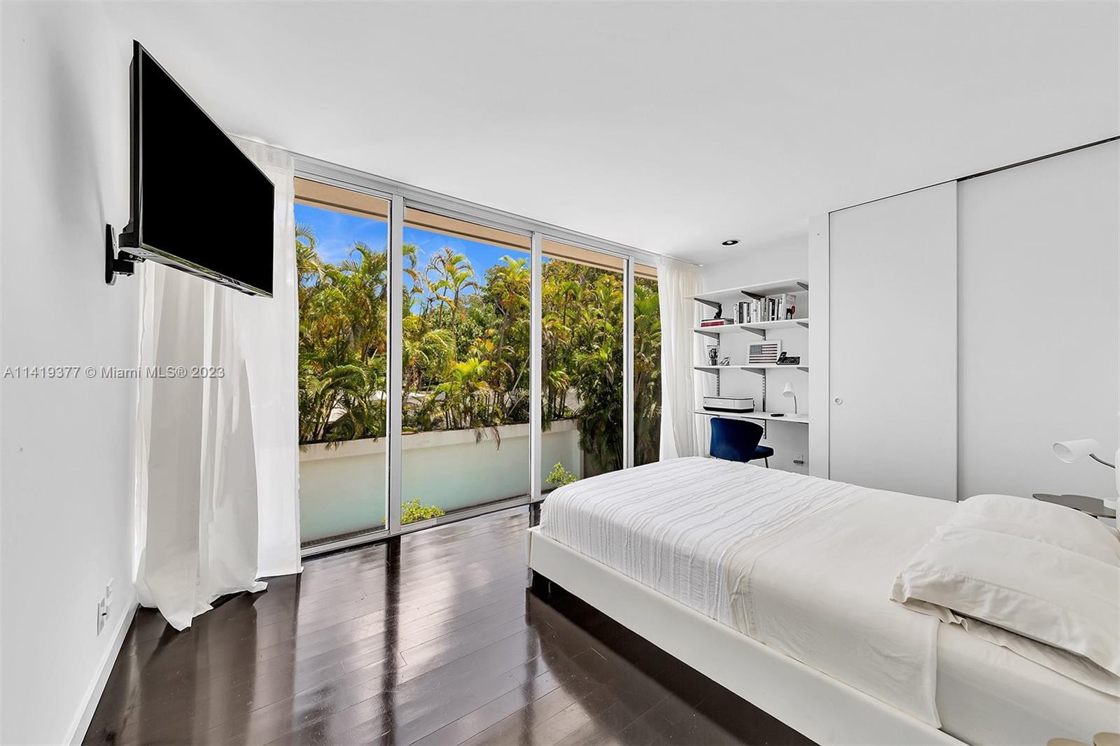 Modern bedroom with a white bed and sliding glass doors overlooking tropical greenery.