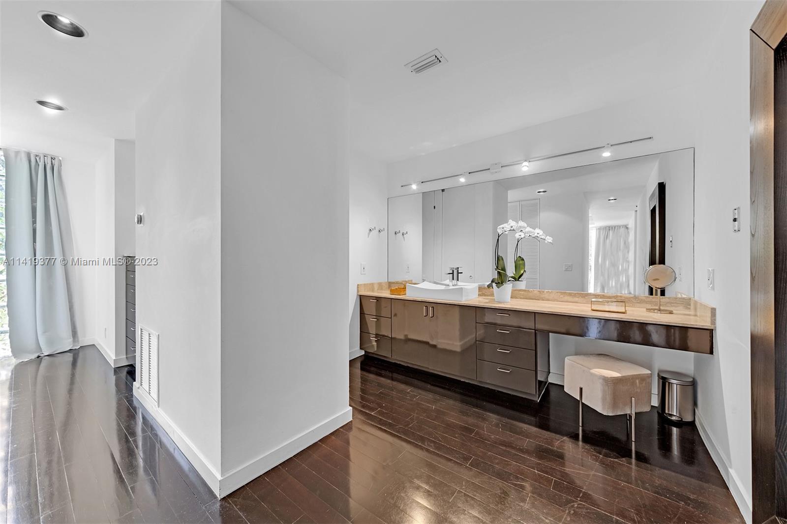 Modern bathroom vanity with a vessel sink, mirrored wall, dark cabinetry, and upholstered stool.