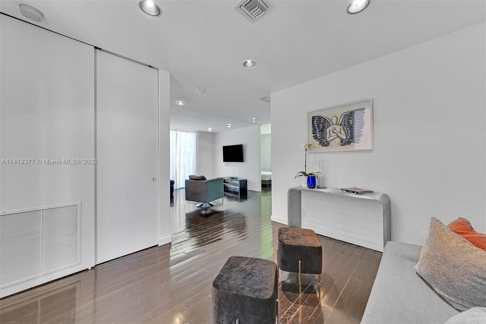 Living room with glossy dark floors, gray seating, and a wall-mounted television.