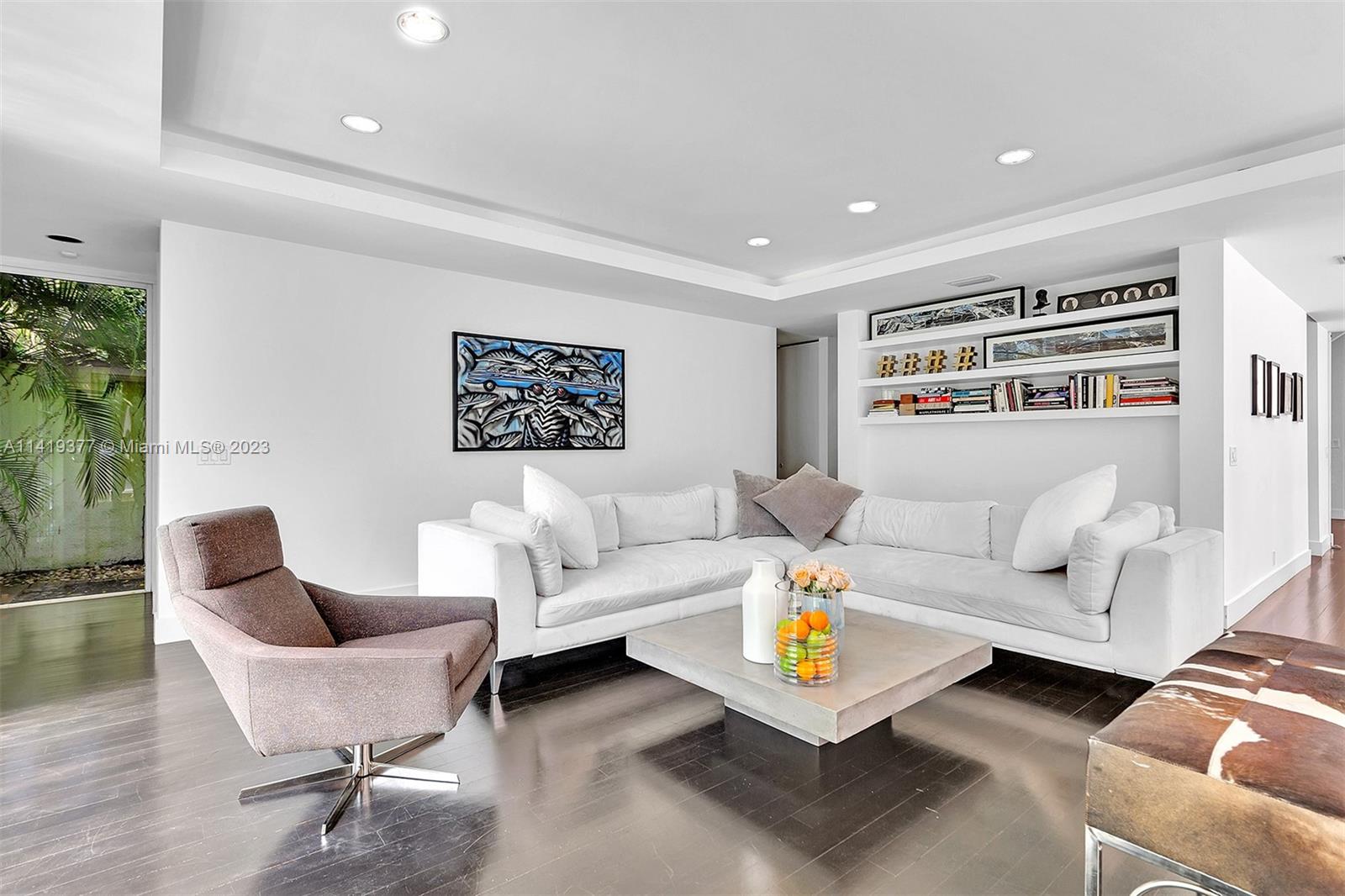 Living room with a white sectional, built-in shelves, dark wood floors, and garden-facing glass doors.