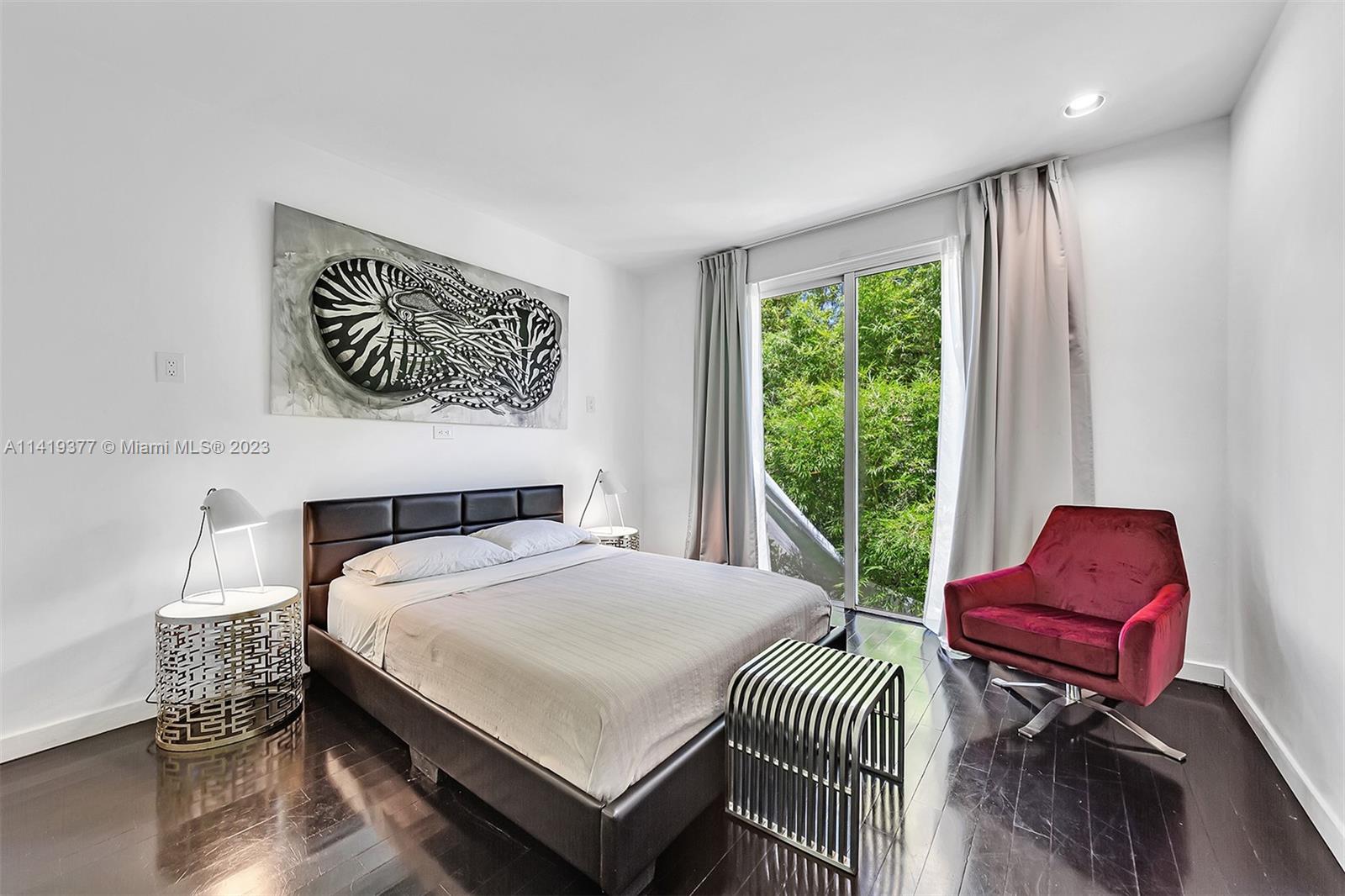 Bedroom with a dark platform bed, red armchair, and sliding glass door overlooking greenery.