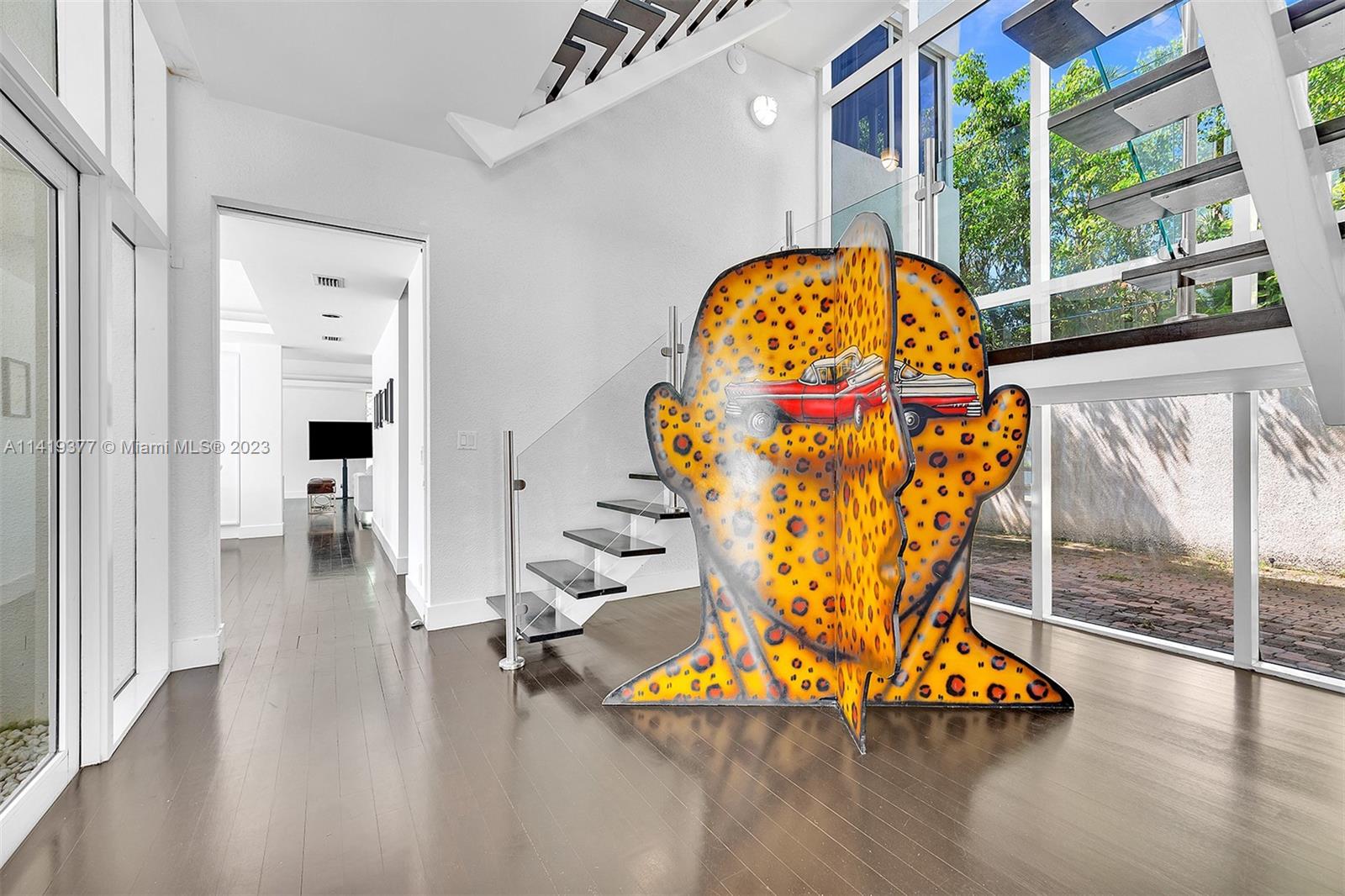 Modern double-height living area with floating staircase, glass walls, and a large spotted orange sculpture.