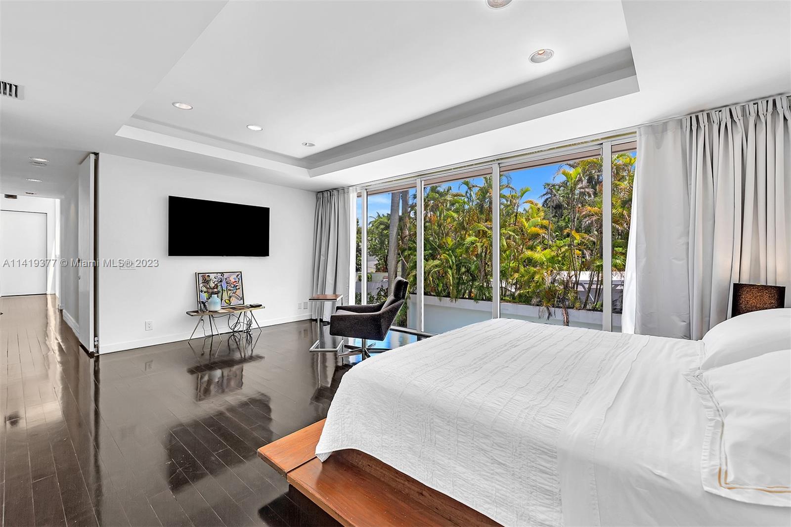 Modern bedroom with white bedding and sliding glass doors overlooking a lush tropical garden.