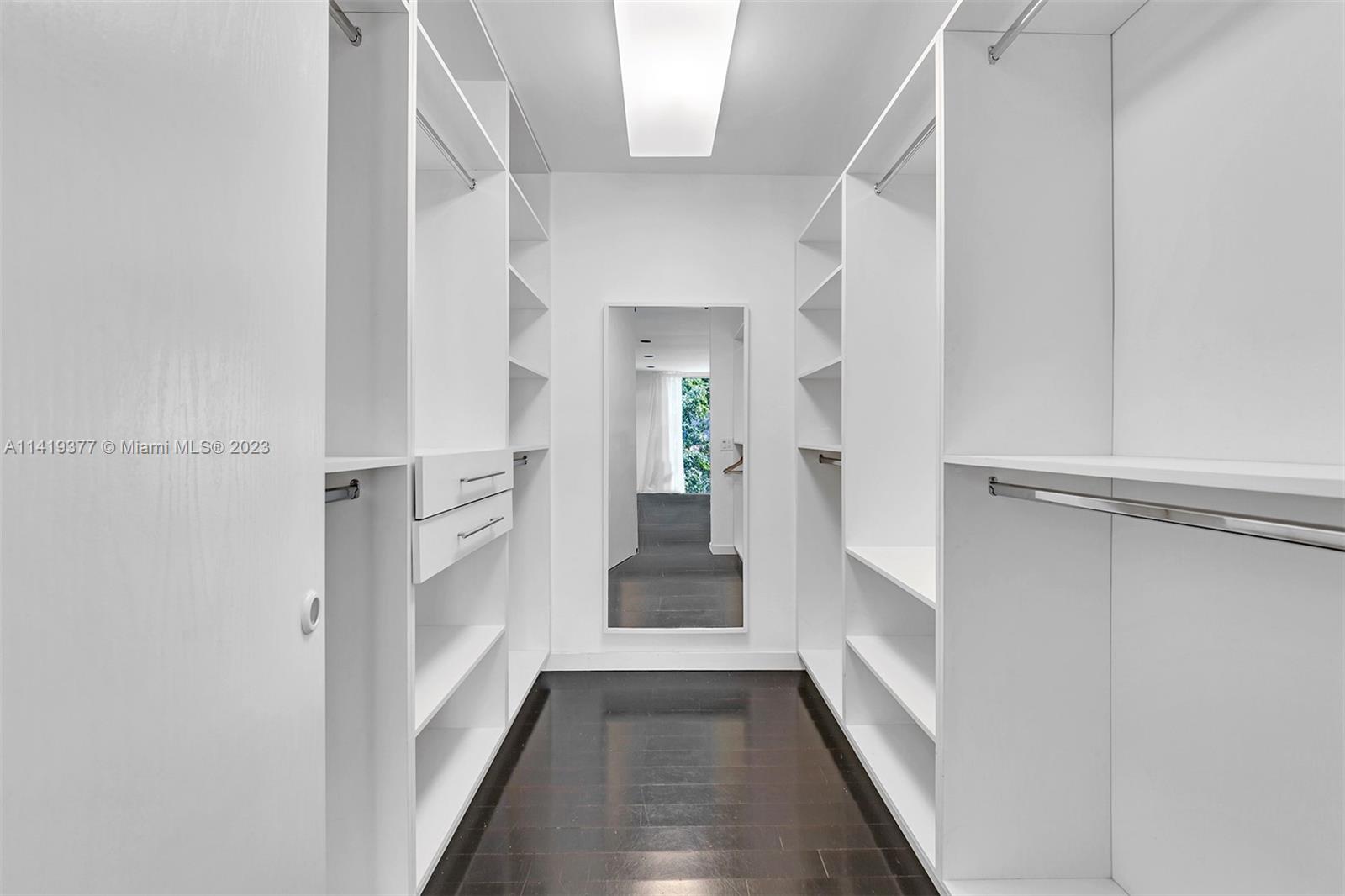 Walk-in closet with white built-in shelving and drawers, dark tile floors, and a full-length mirror.