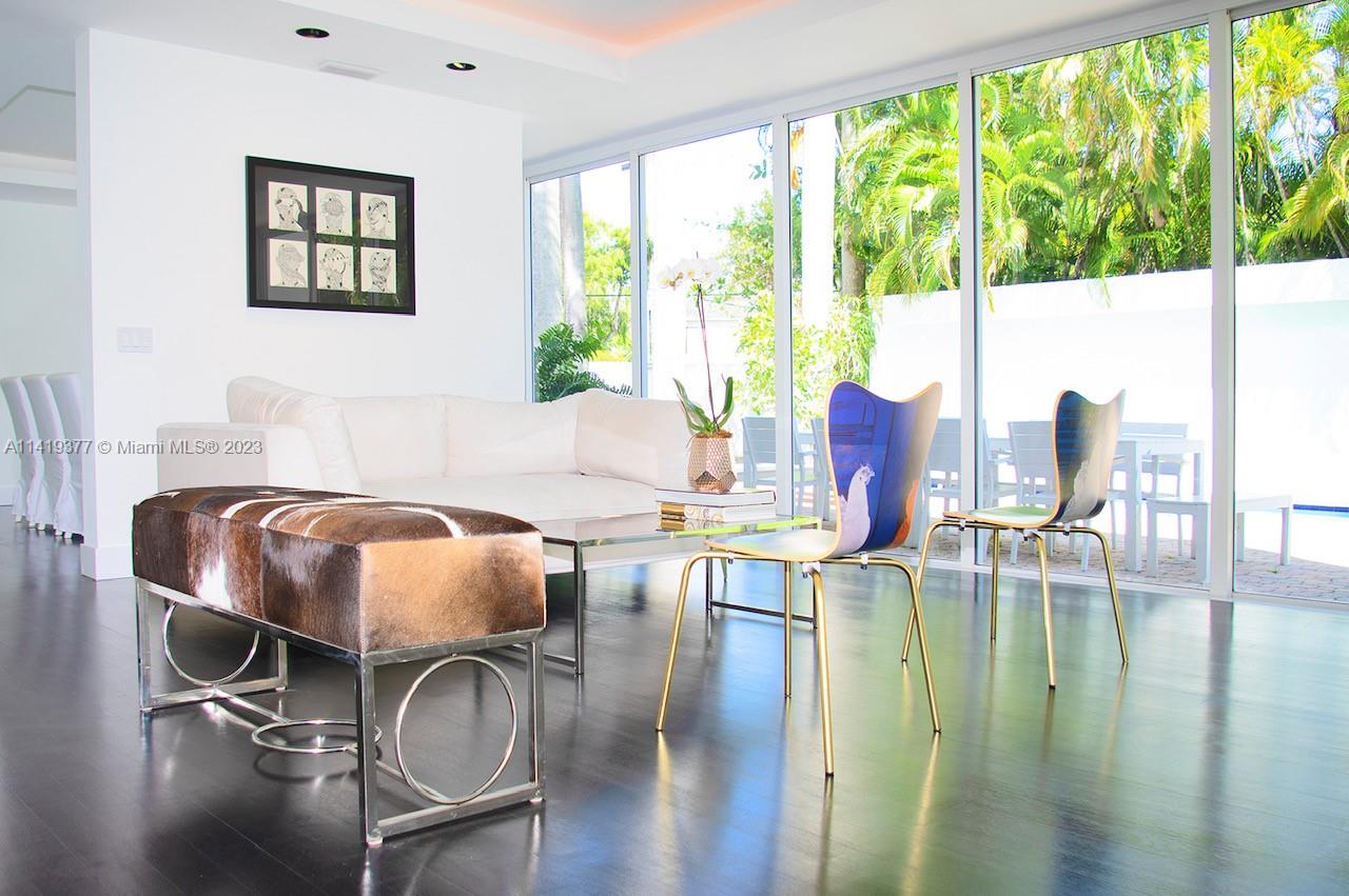 Modern living room with a white sectional, sculptural chairs, and floor-to-ceiling windows overlooking a tropical patio.