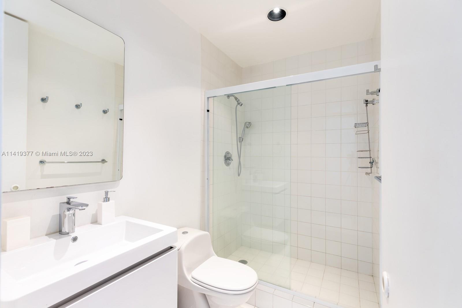 White bathroom with a glass shower, tiled walls, vanity sink, and toilet.