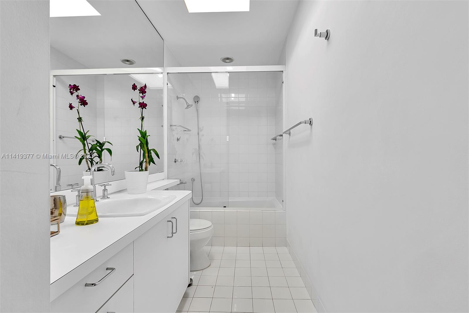 White bathroom with a long vanity and mirrored sliding doors on the tub-shower.
