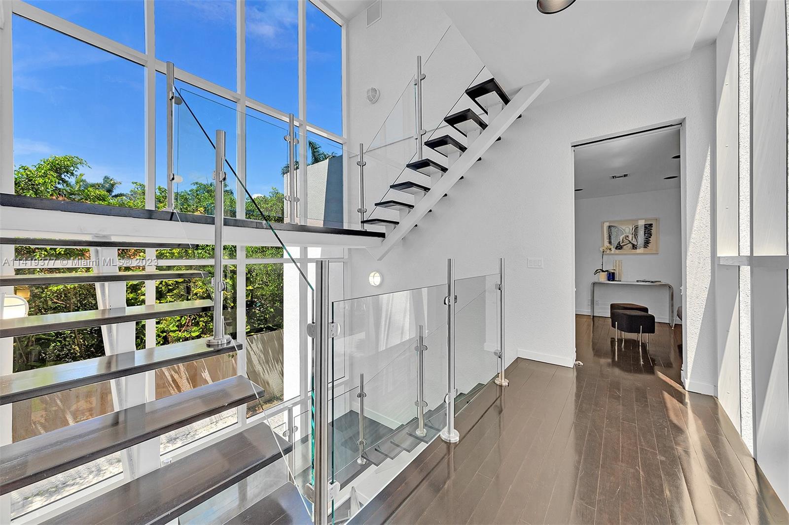 Double-height foyer with a floating staircase, glass railings, and tall windows.