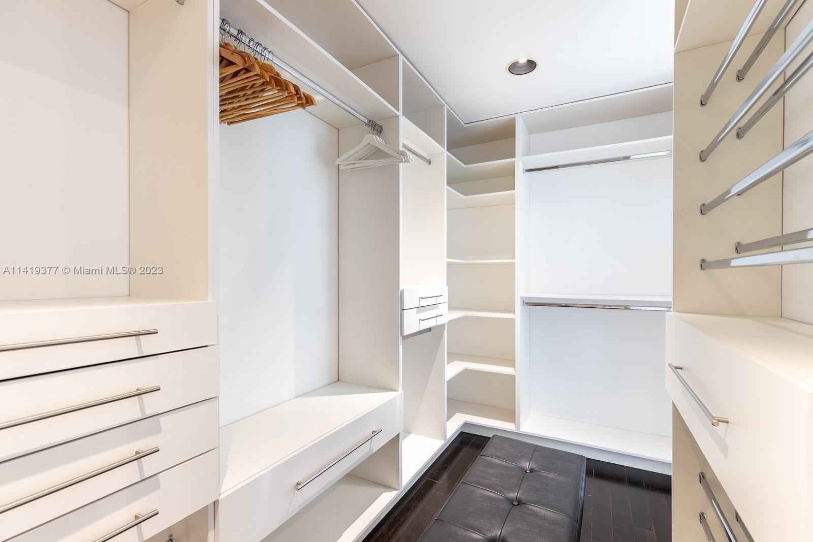Walk-in closet with white built-ins, wooden hangers, and a dark cushioned bench.