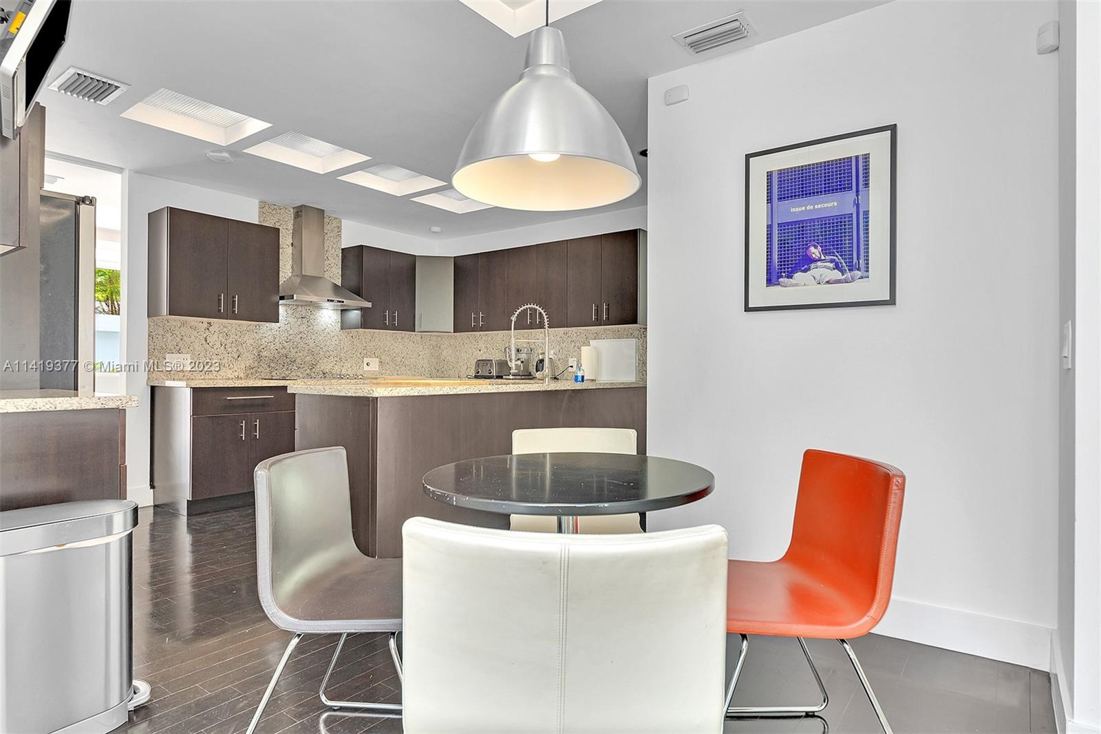 Kitchen and dining area with dark cabinets, granite counters, and a round table with white and orange chairs.
