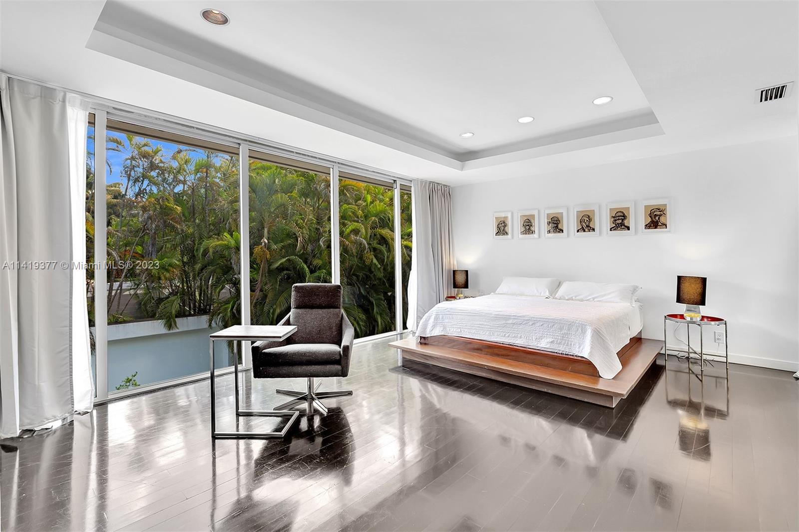 Bedroom with a platform bed and floor-to-ceiling glass doors overlooking tropical greenery.