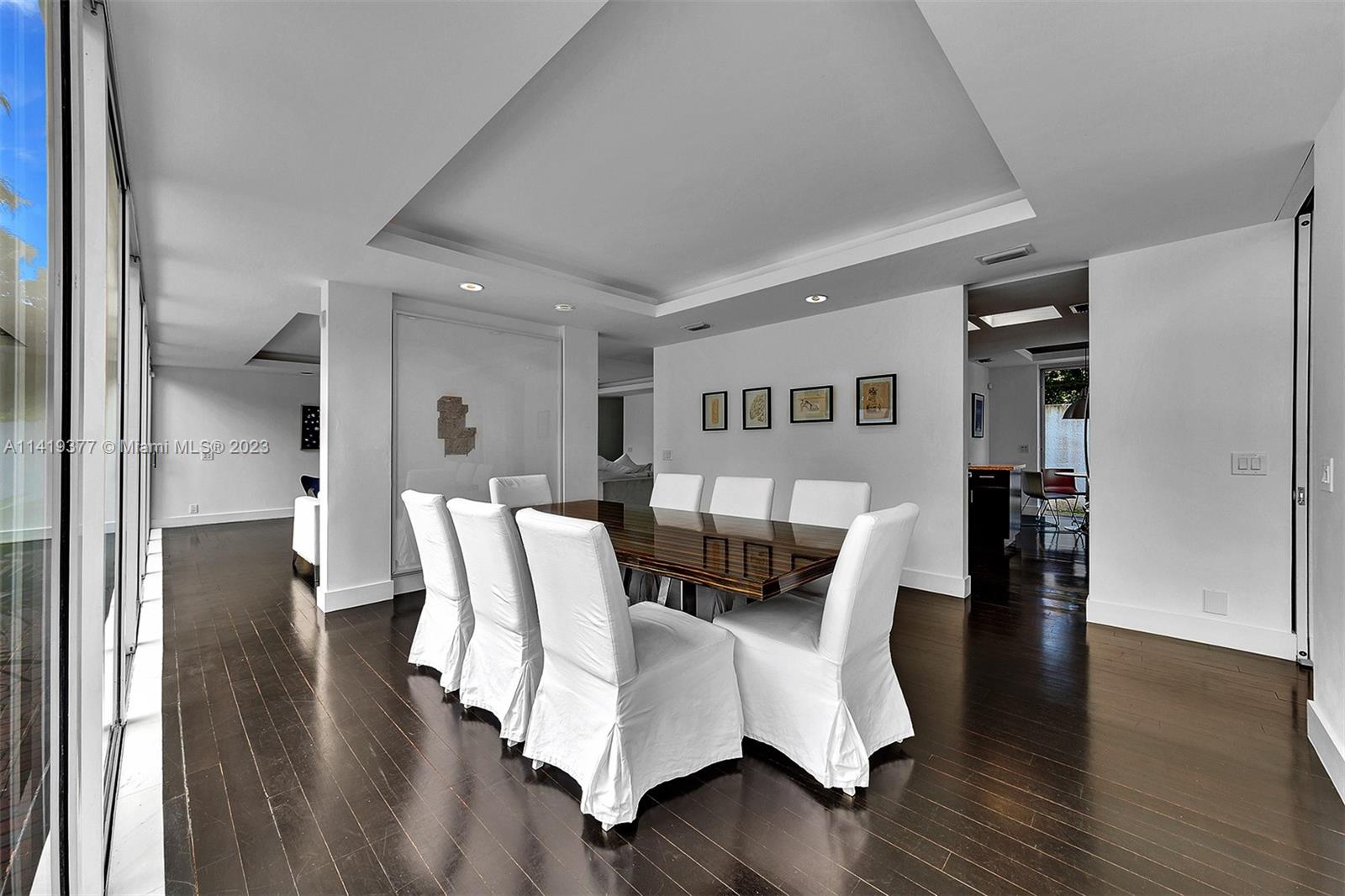 Dining room with a dark wood table, white chairs, and sliding glass doors.