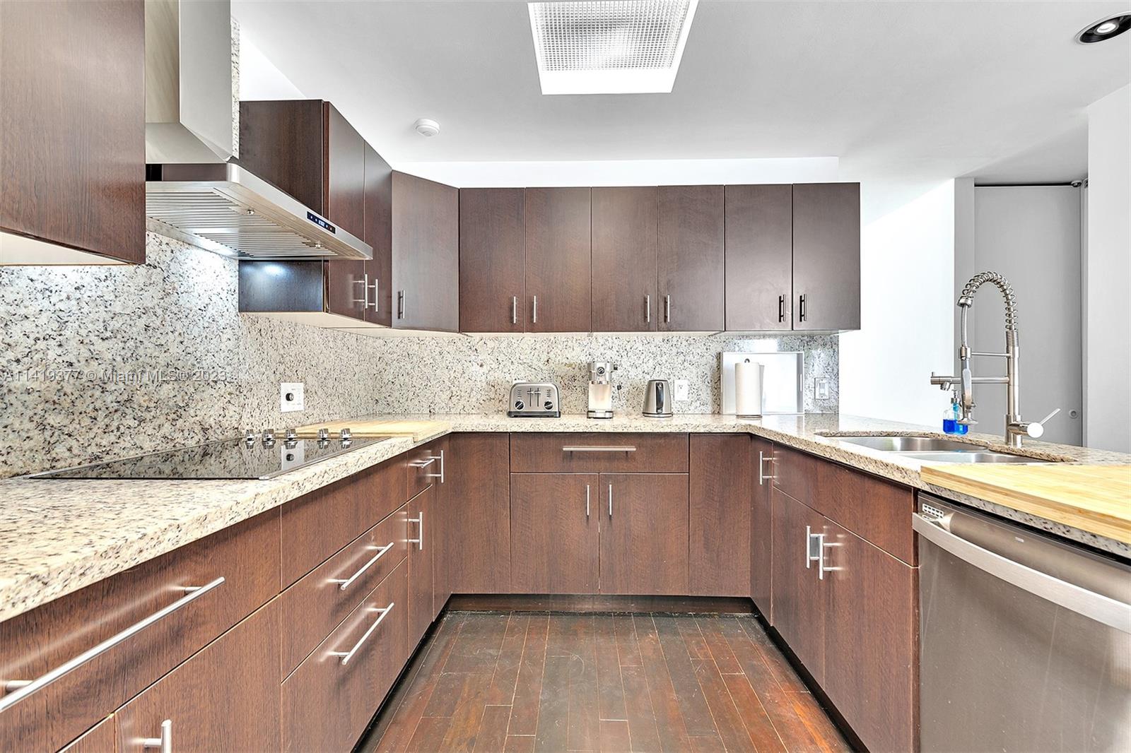 U-shaped kitchen with dark wood cabinets, granite counters, and a deep sink with a spring-coil faucet.
