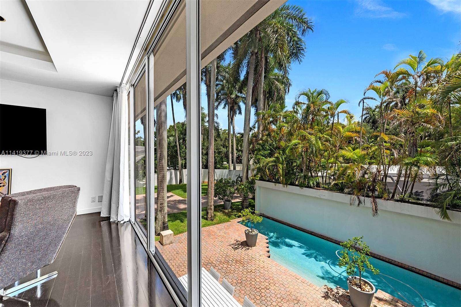 Interior with sliding glass doors overlooking a swimming pool and tropical garden.