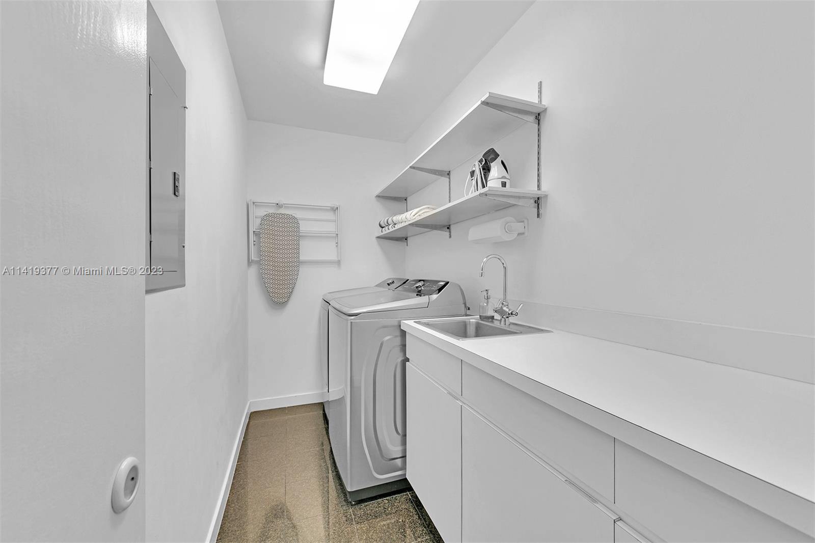Laundry room with washer and dryer, utility sink, long white counter, and open shelving.