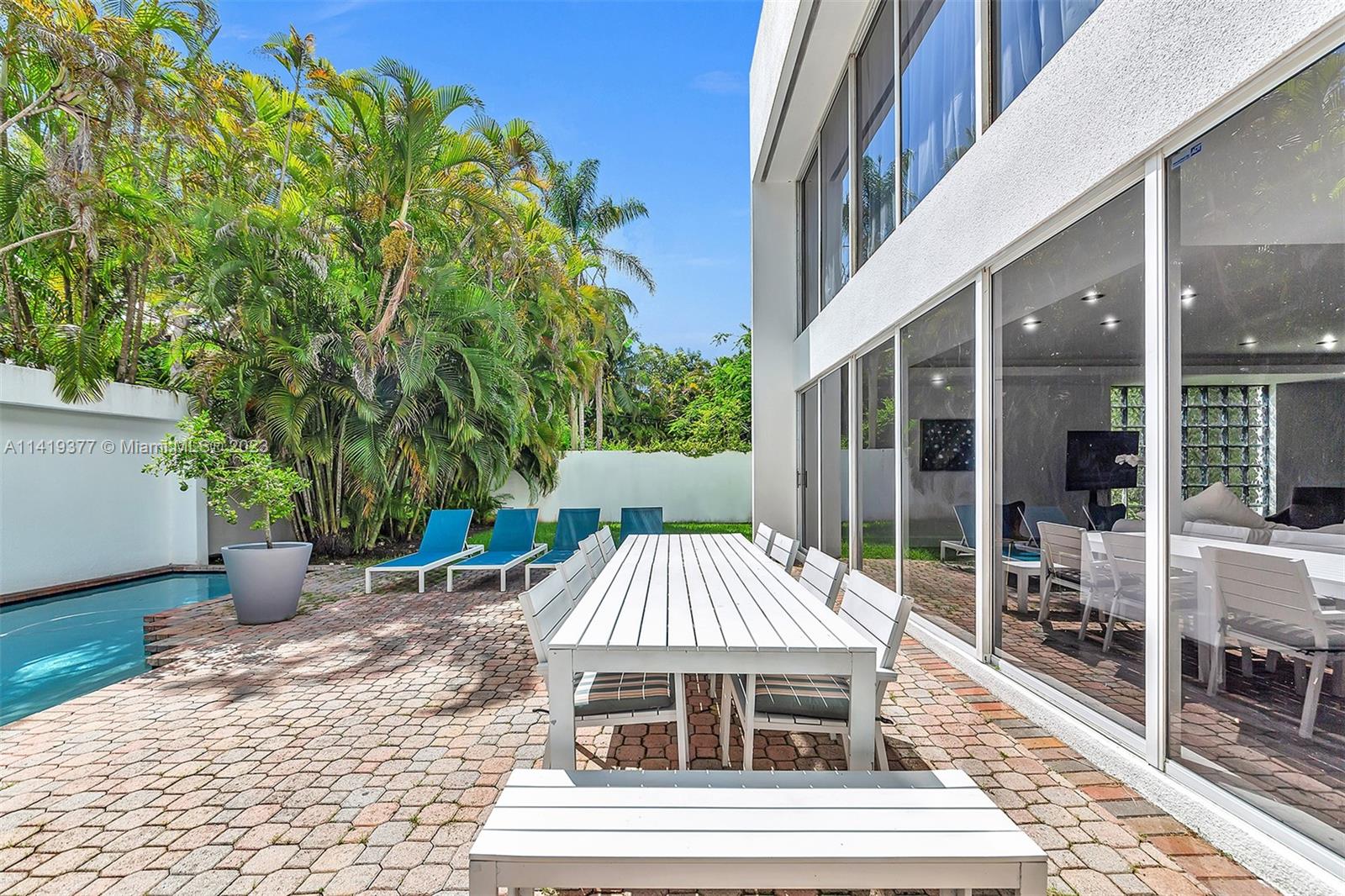 Modern home patio with outdoor dining set, swimming pool, and tropical palms.