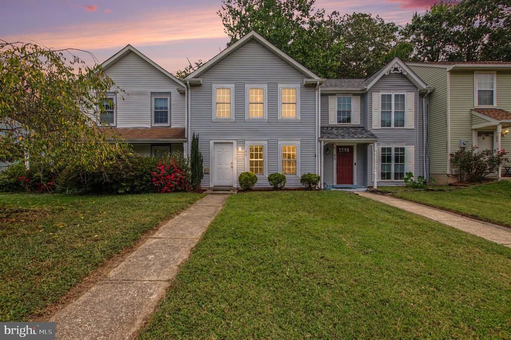 Gray two-story townhouse with a red front door and glowing windows at dusk.