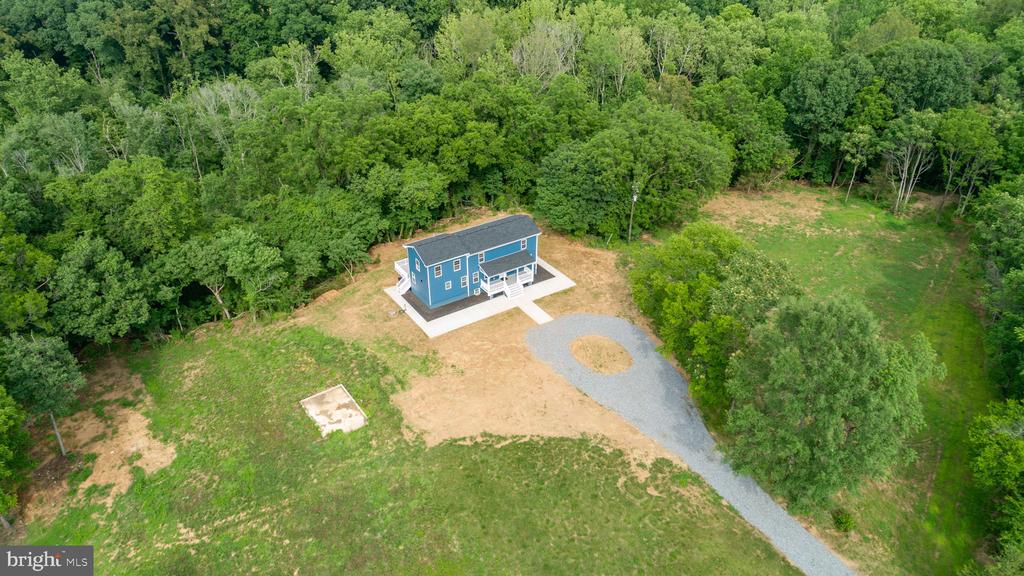 Aerial view of a blue two-story house and curved gravel driveway on a wooded lot.