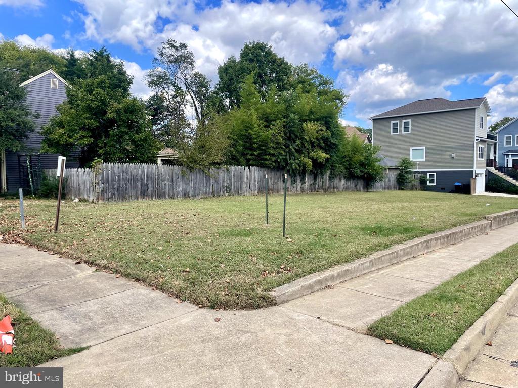 Grassy vacant lot bordered by a wooden fence, trees, and neighboring homes.